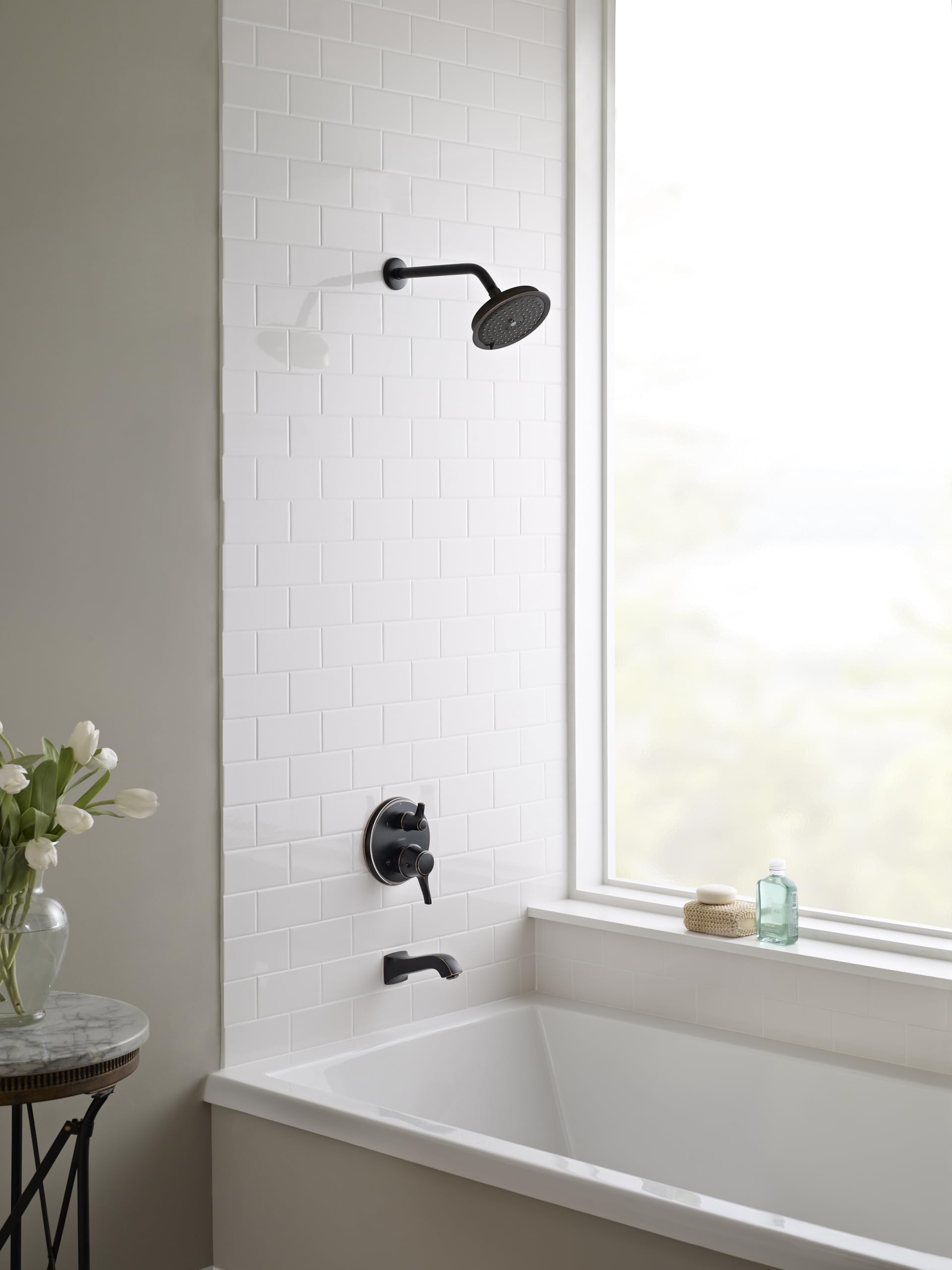 Rubbed bronze shower head with curved arm mounted on white subway tile wall above bathtub.