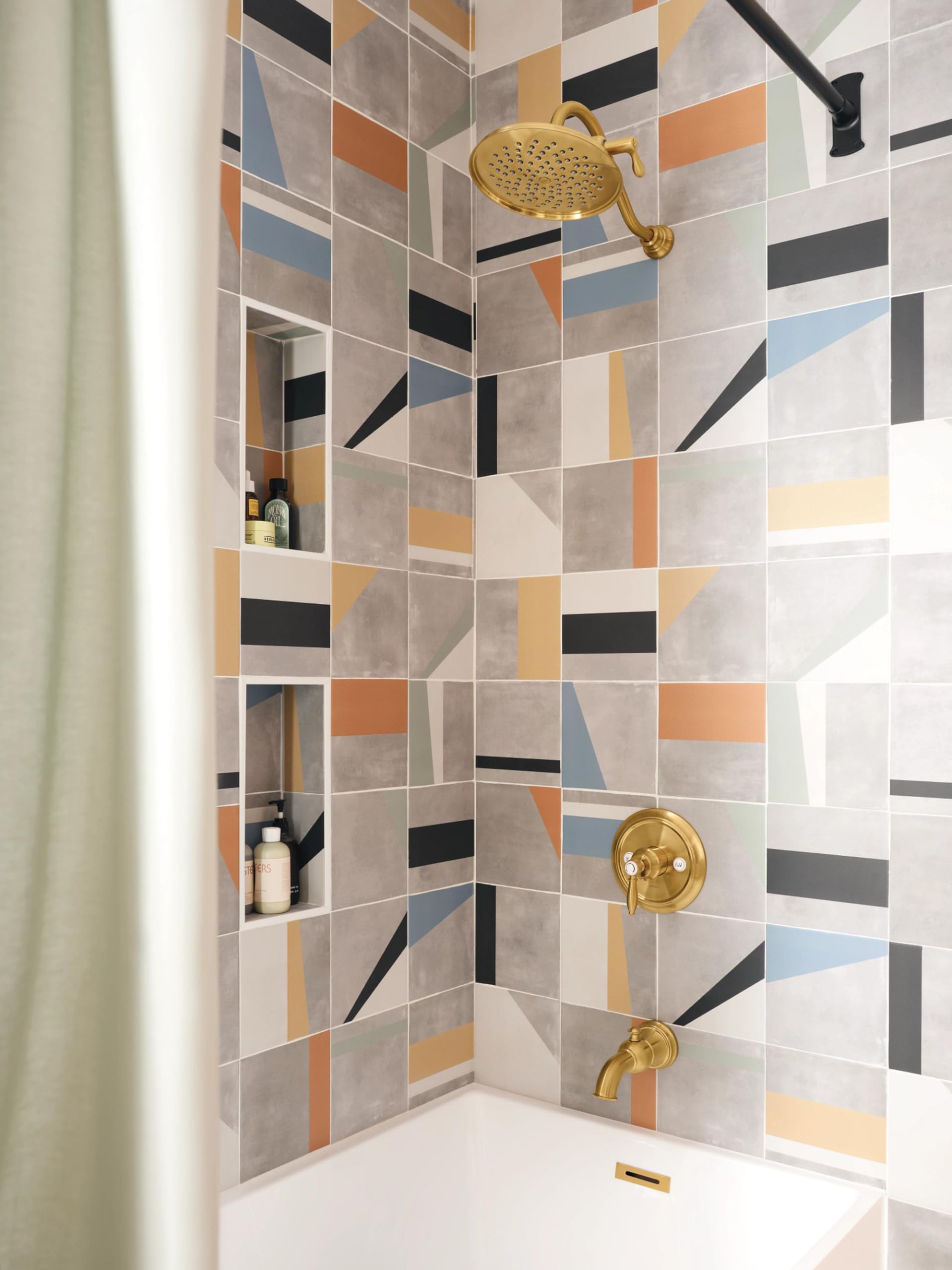 Brushed gold tub and shower trim with single handle, showerhead, and spout mounted on geometric patterned tile wall.