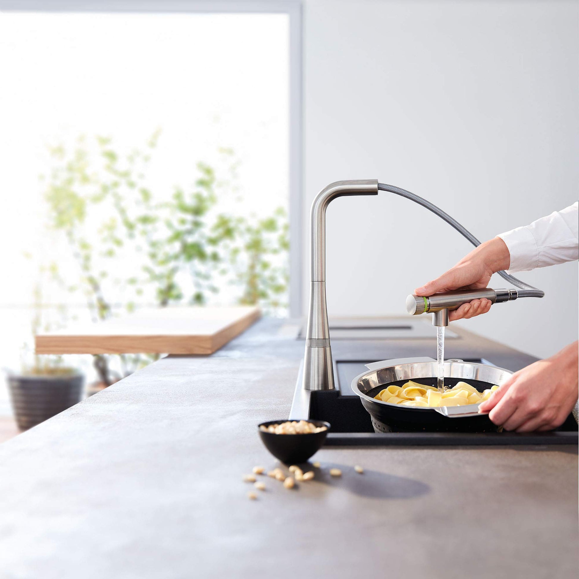 Grohe Zedra stainless steel pull-out kitchen faucet with flexible hose spraying water into a pan of food.