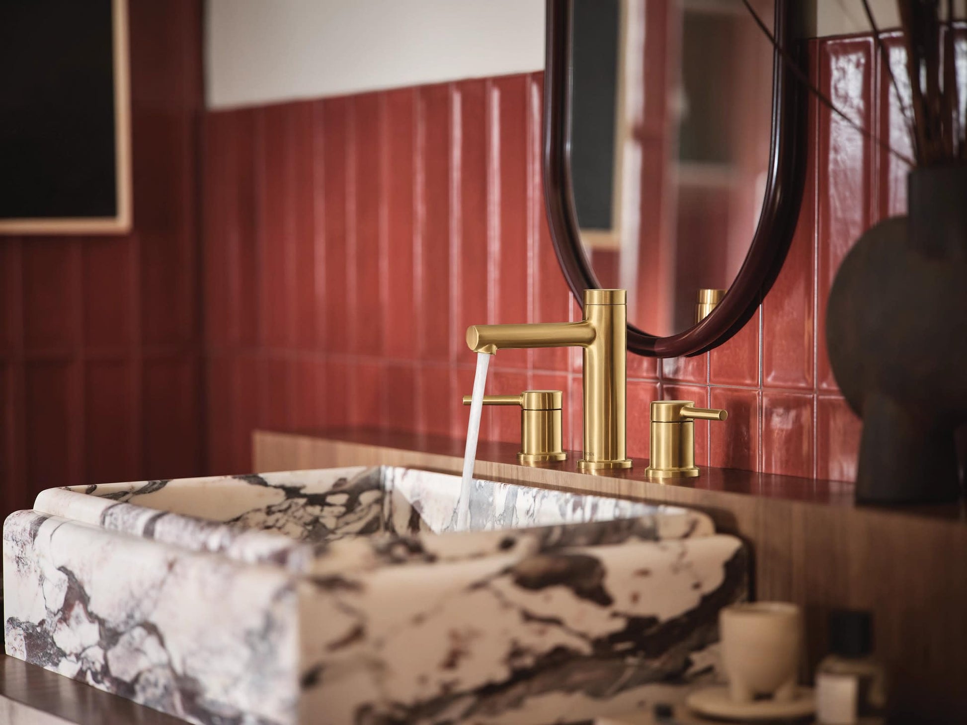 Brushed gold two-handle widespread faucet trim with cylindrical spout installed above marble sink.