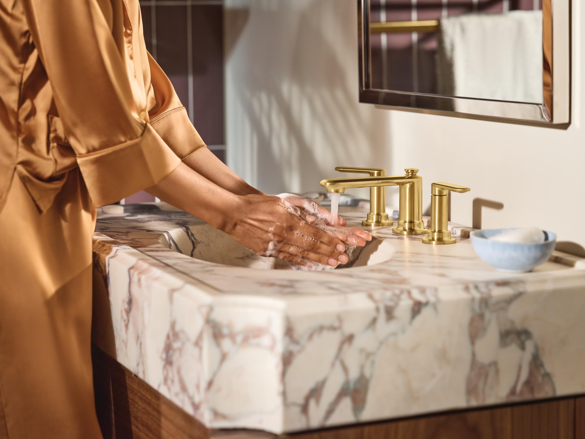 Brushed gold two-handle widespread faucet installed on marble bathroom sink with water running.
