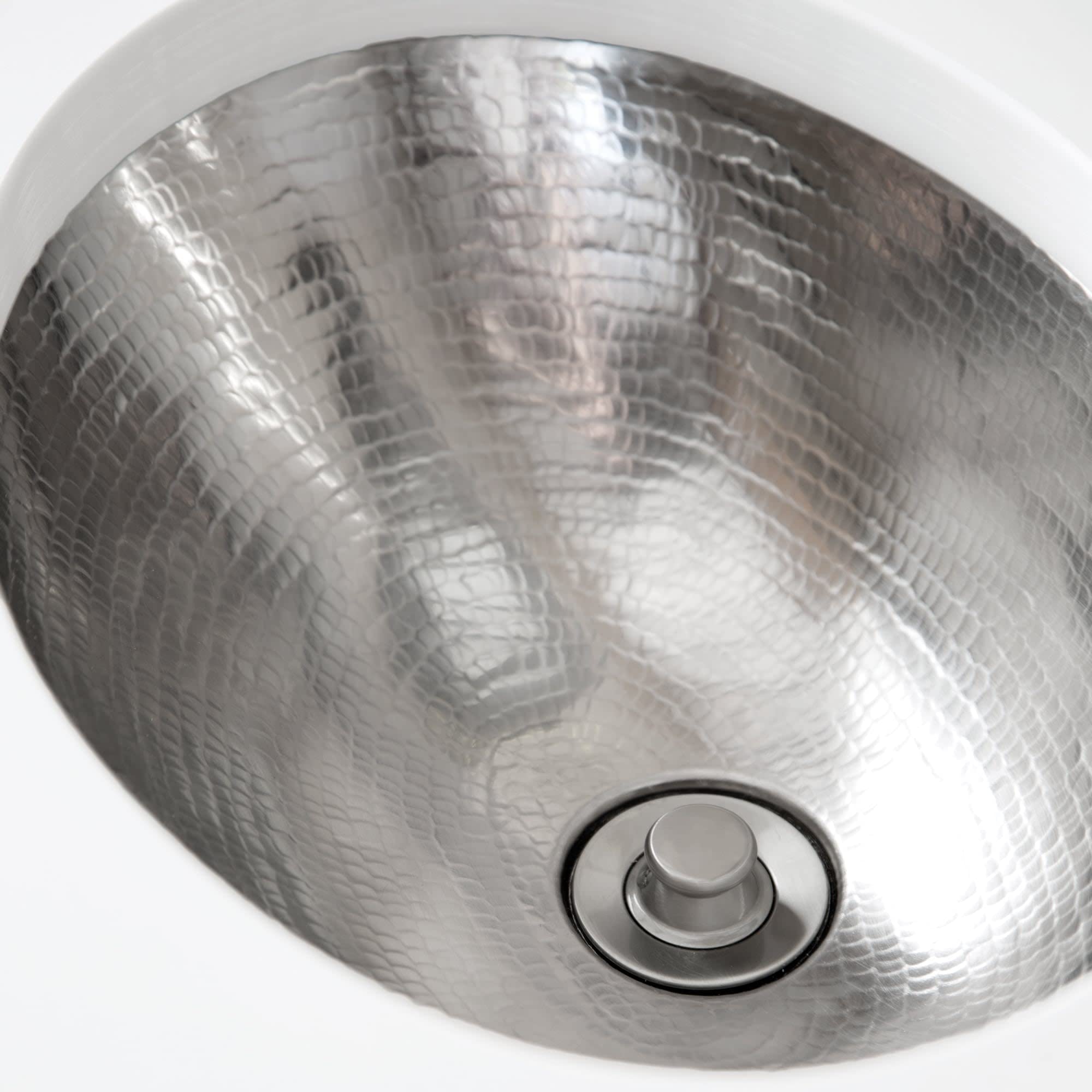 Hammered copper bathroom sink with crosshatch texture pattern and chrome drain fixture, viewed from above.