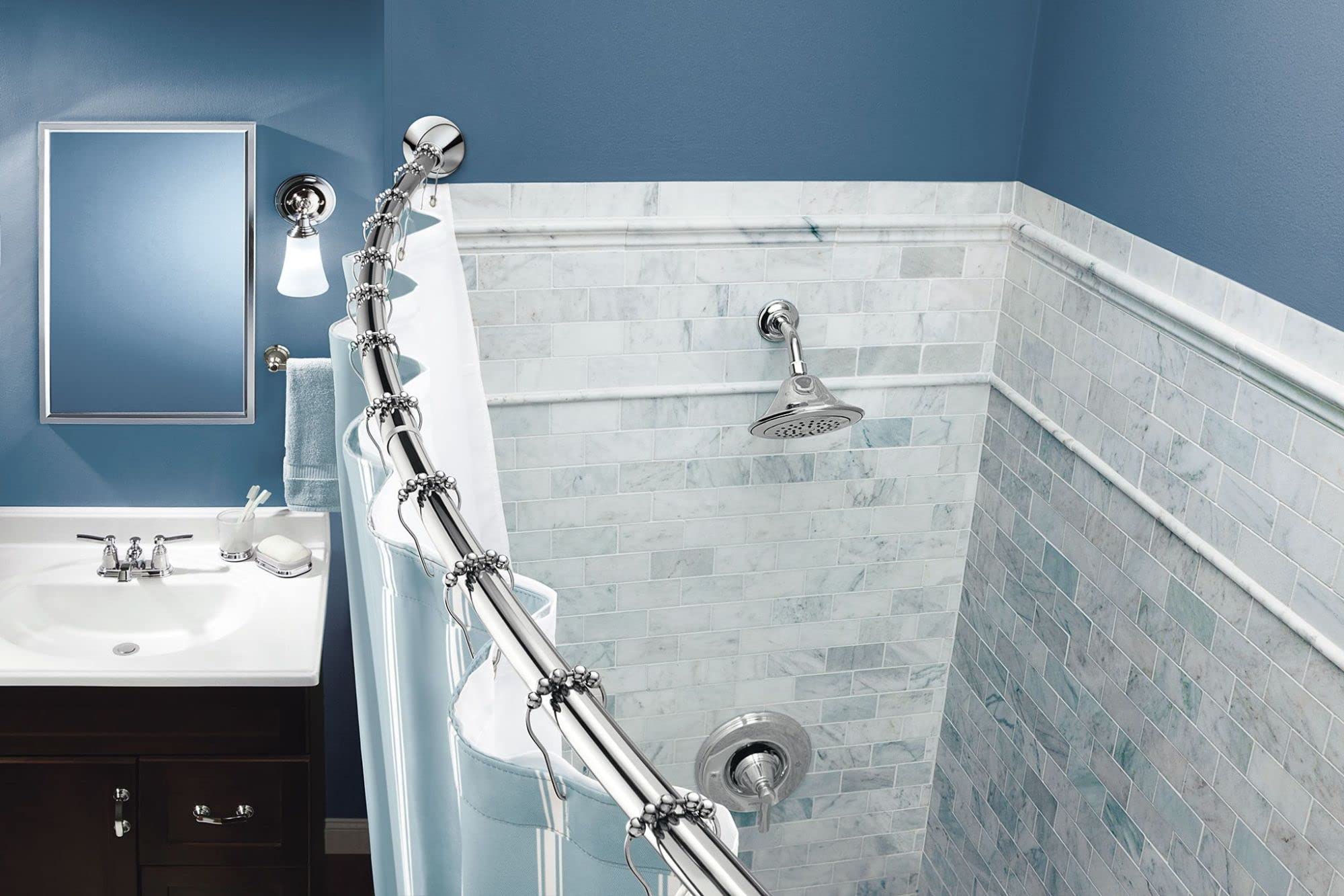 Curved chrome shower rod with white shower curtain installed in bathroom above tiled shower enclosure.