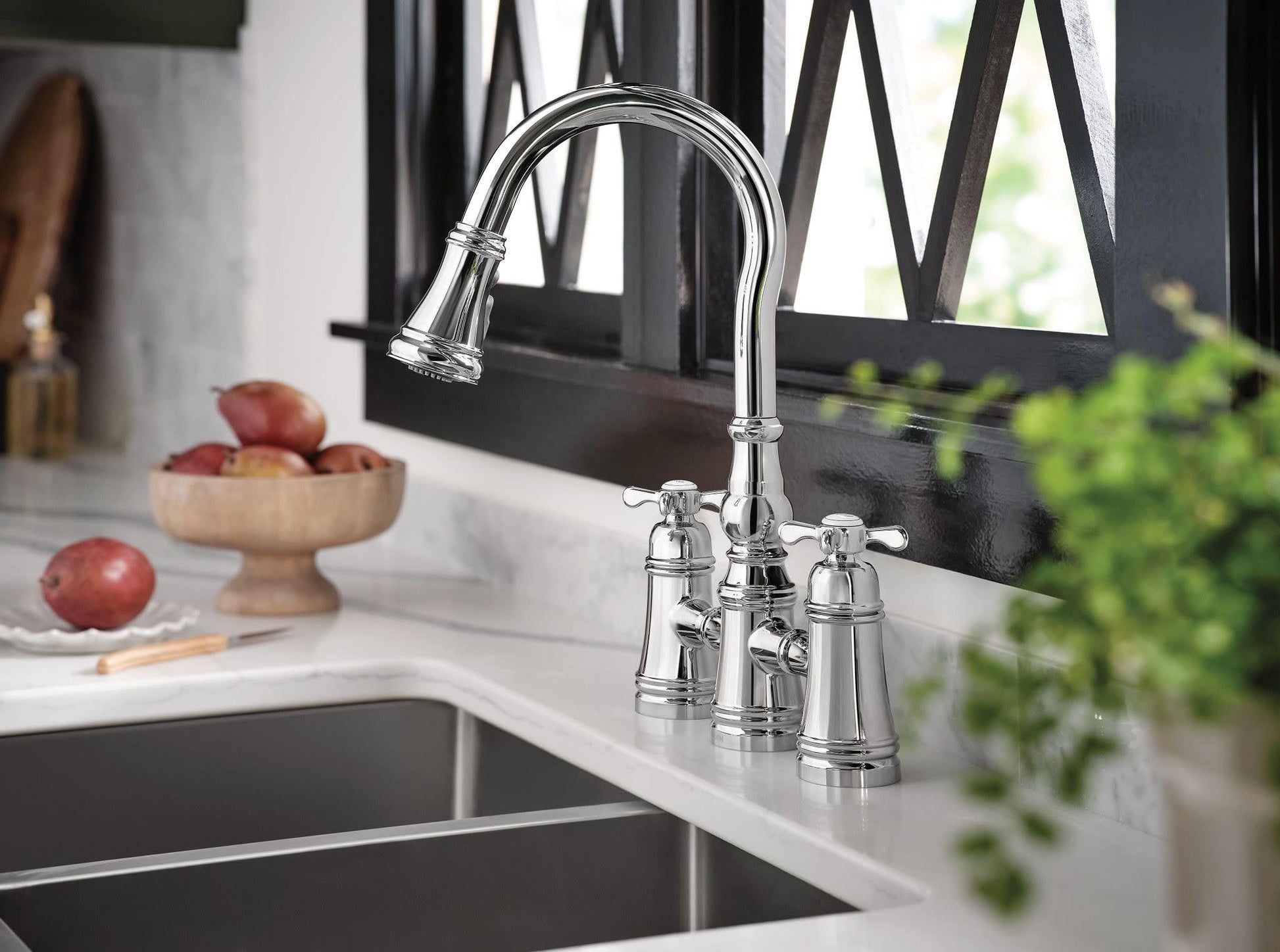 Chrome two-handle pulldown bridge kitchen faucet with curved spout installed above sink.