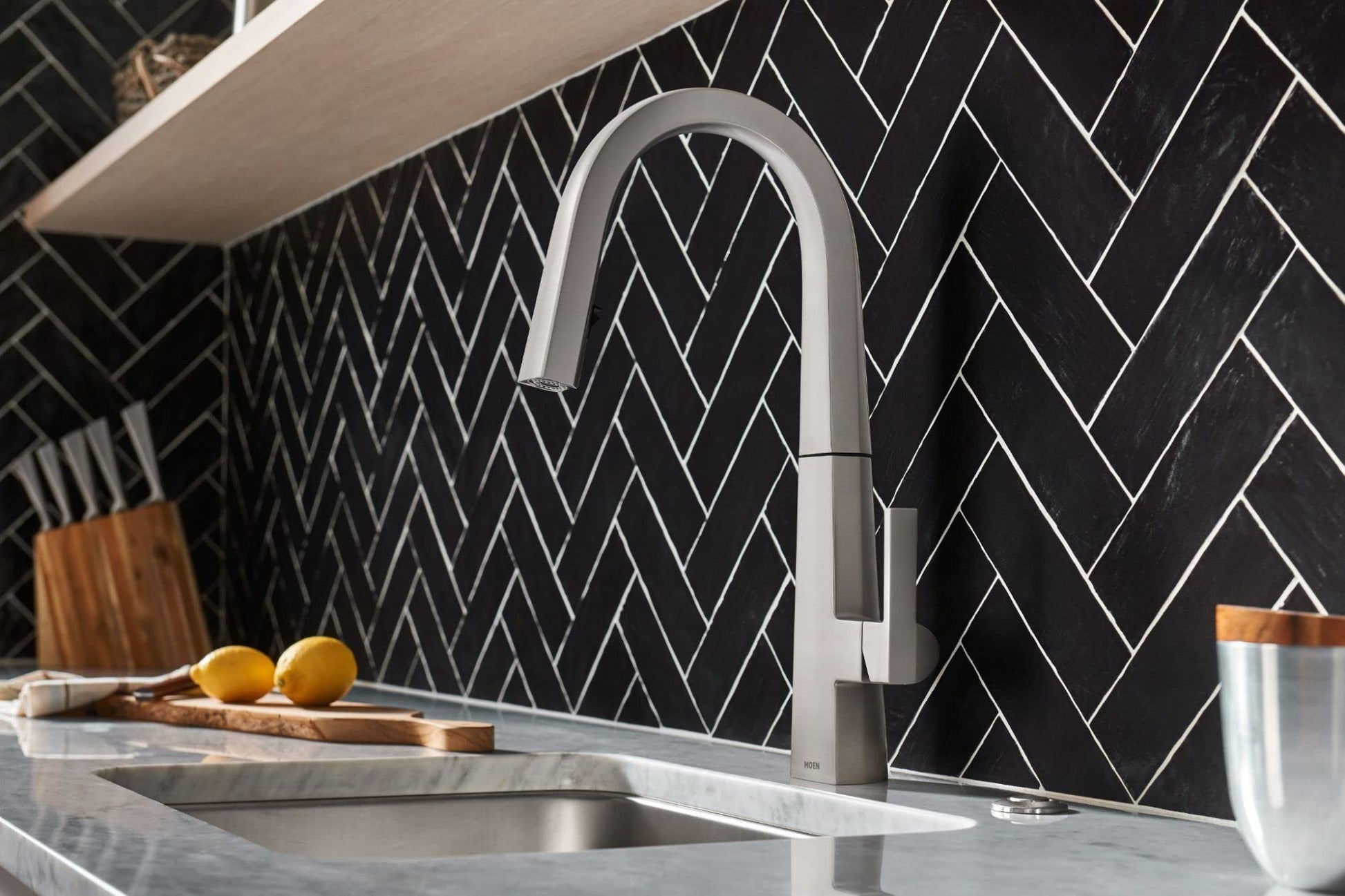 Stainless steel pull-down kitchen faucet with curved spout and single handle mounted above sink with herringbone tile backspl