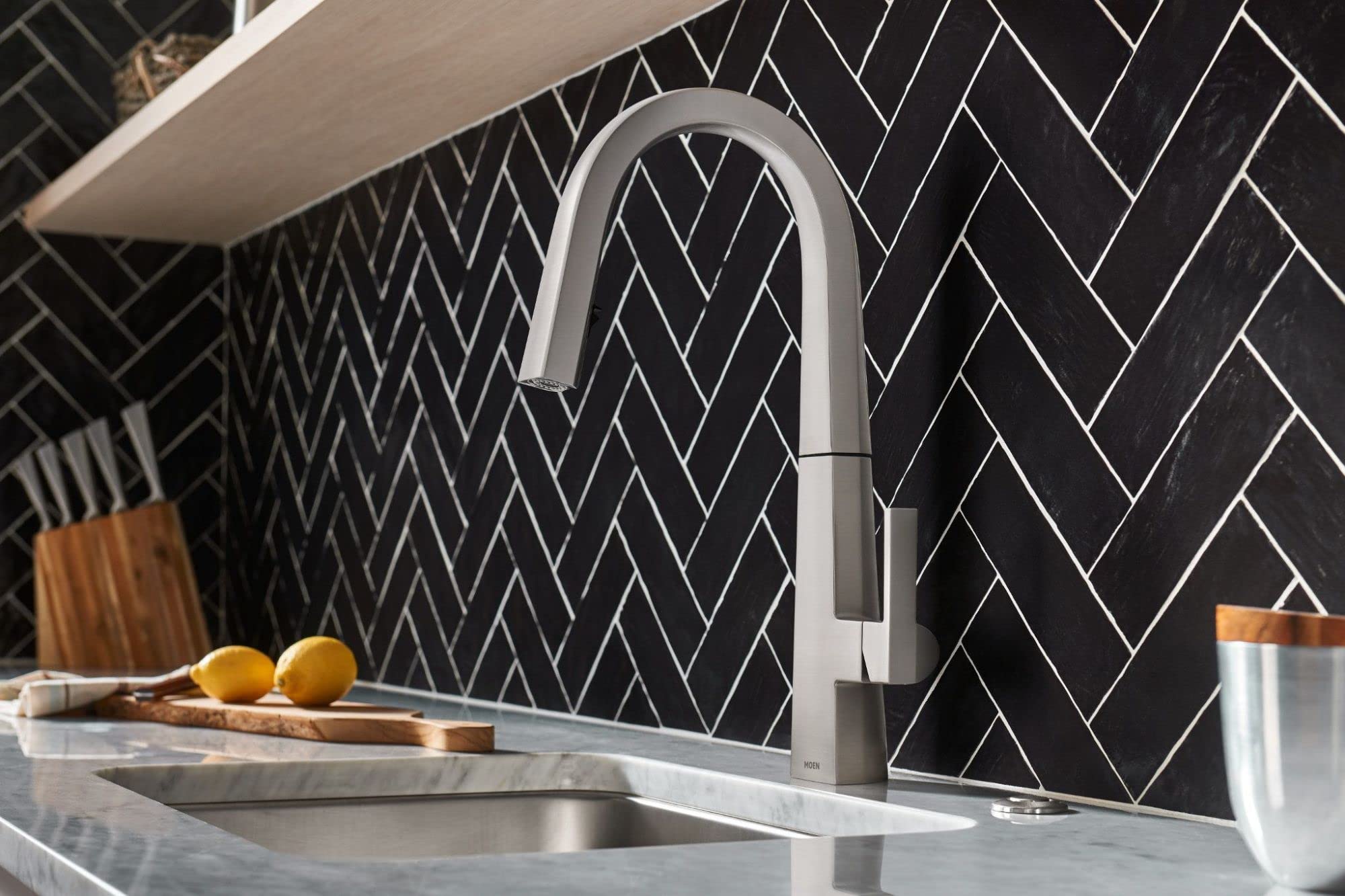 Stainless steel pull-down kitchen faucet with curved spout and single handle mounted above sink with herringbone tile backspl