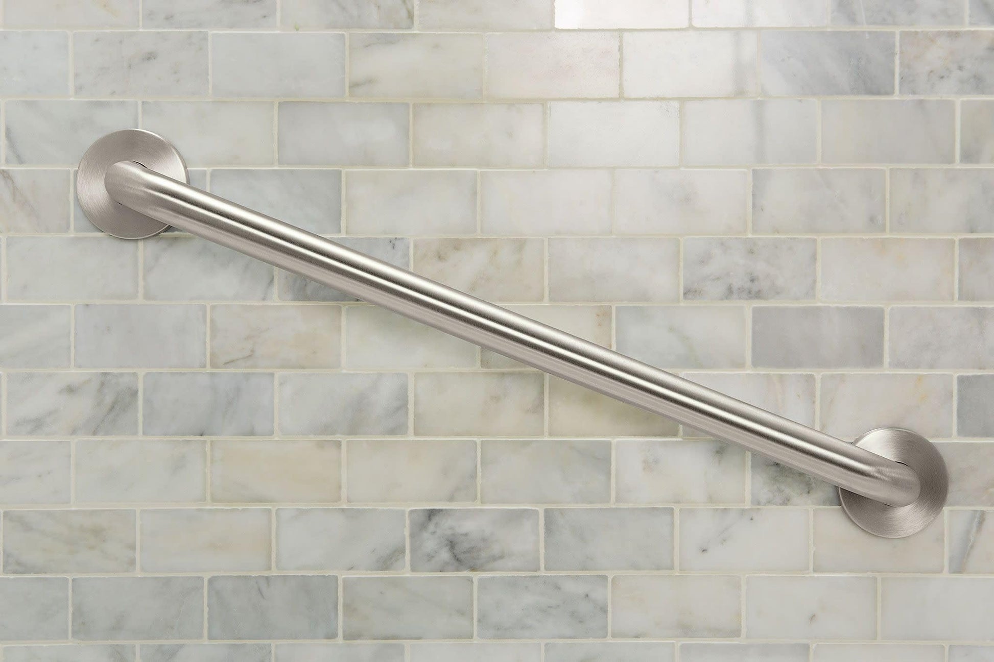 Stainless steel grab bar with circular wall mounts installed on marble subway tile.