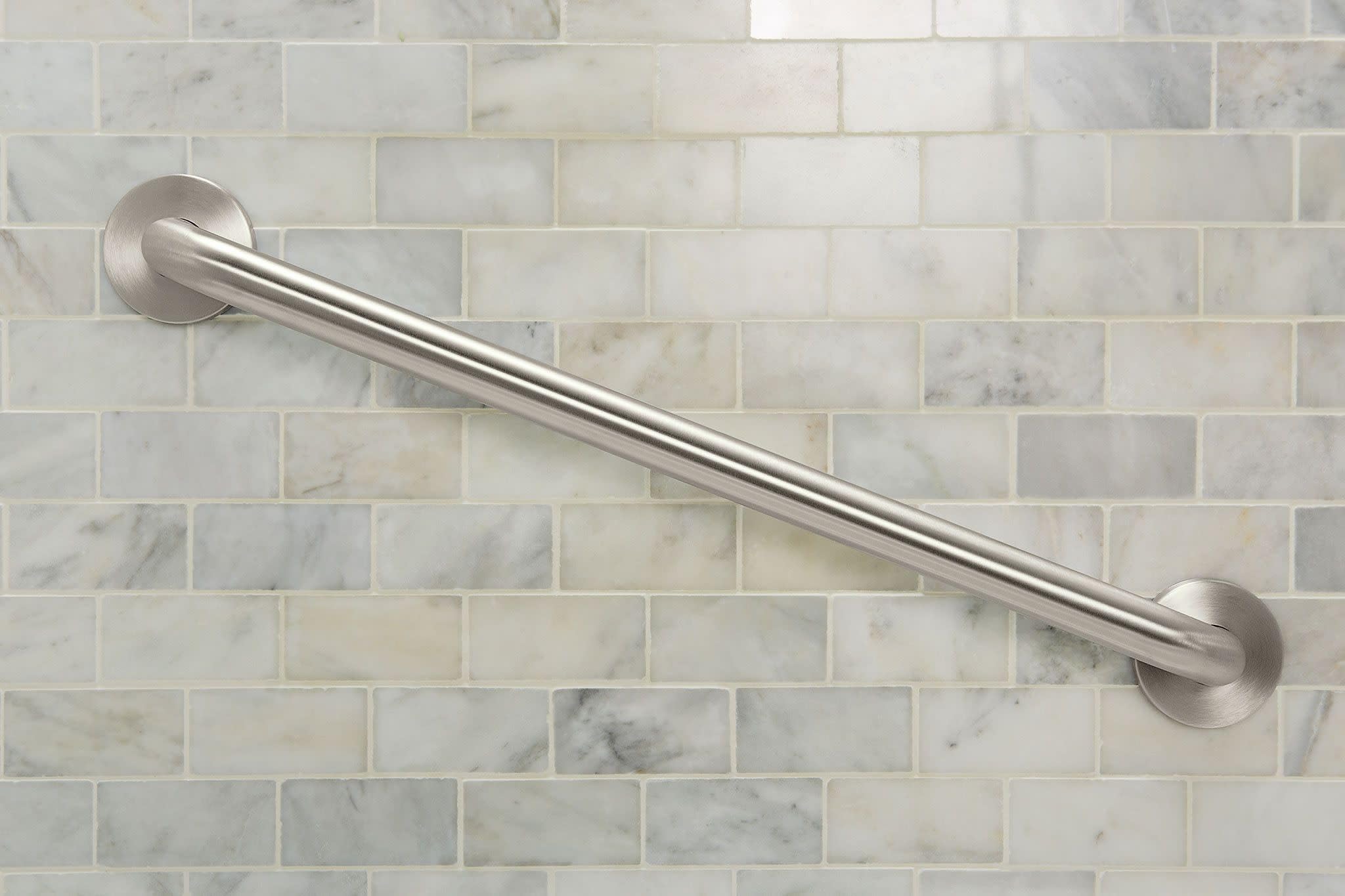 Stainless steel grab bar with circular wall mounts installed on marble subway tile.