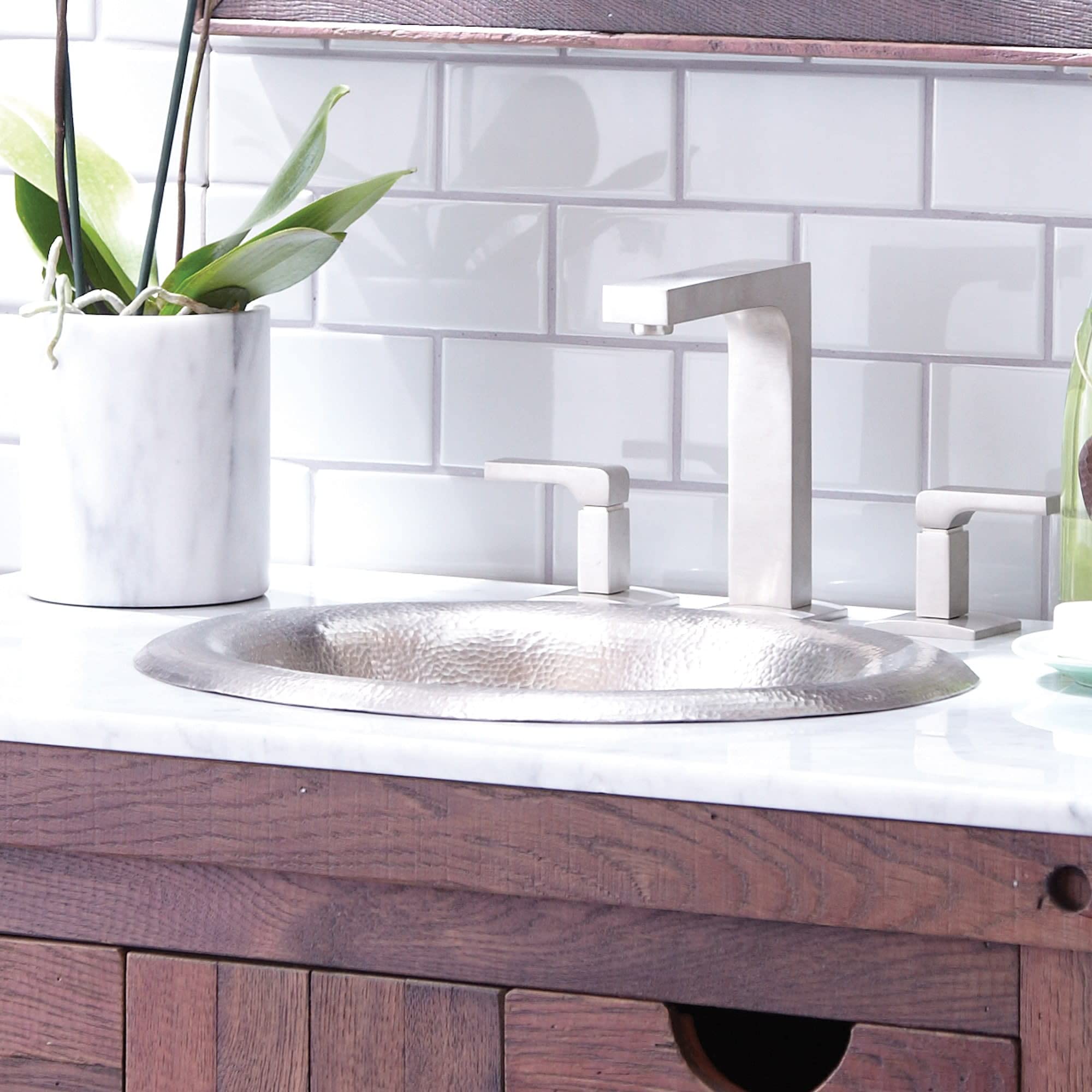 Hammered metal lotus-shaped sink with geometric faucet and handles on white marble countertop.