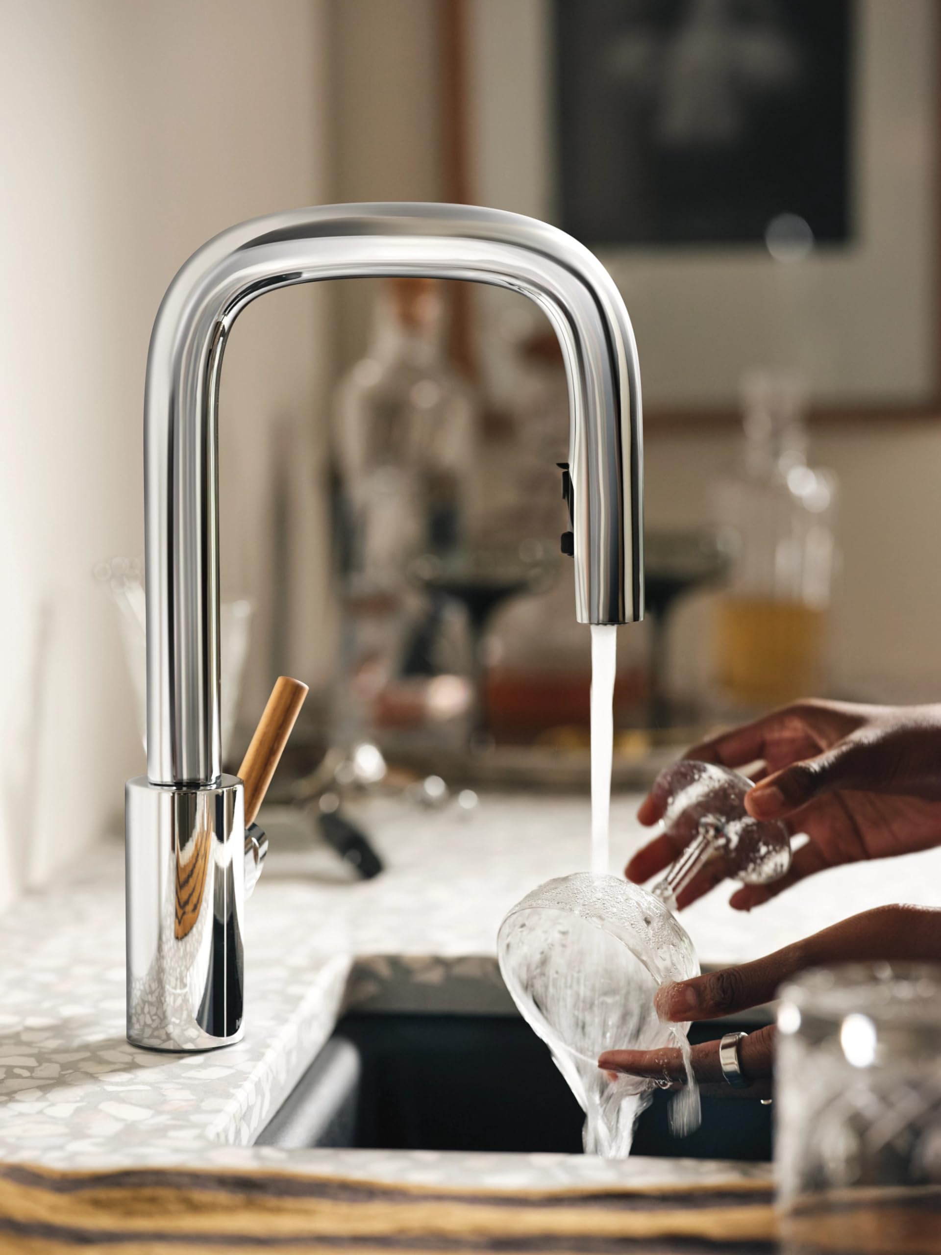 Chrome bar faucet with pulldown sprayer and wooden handle installed on kitchen sink counter.