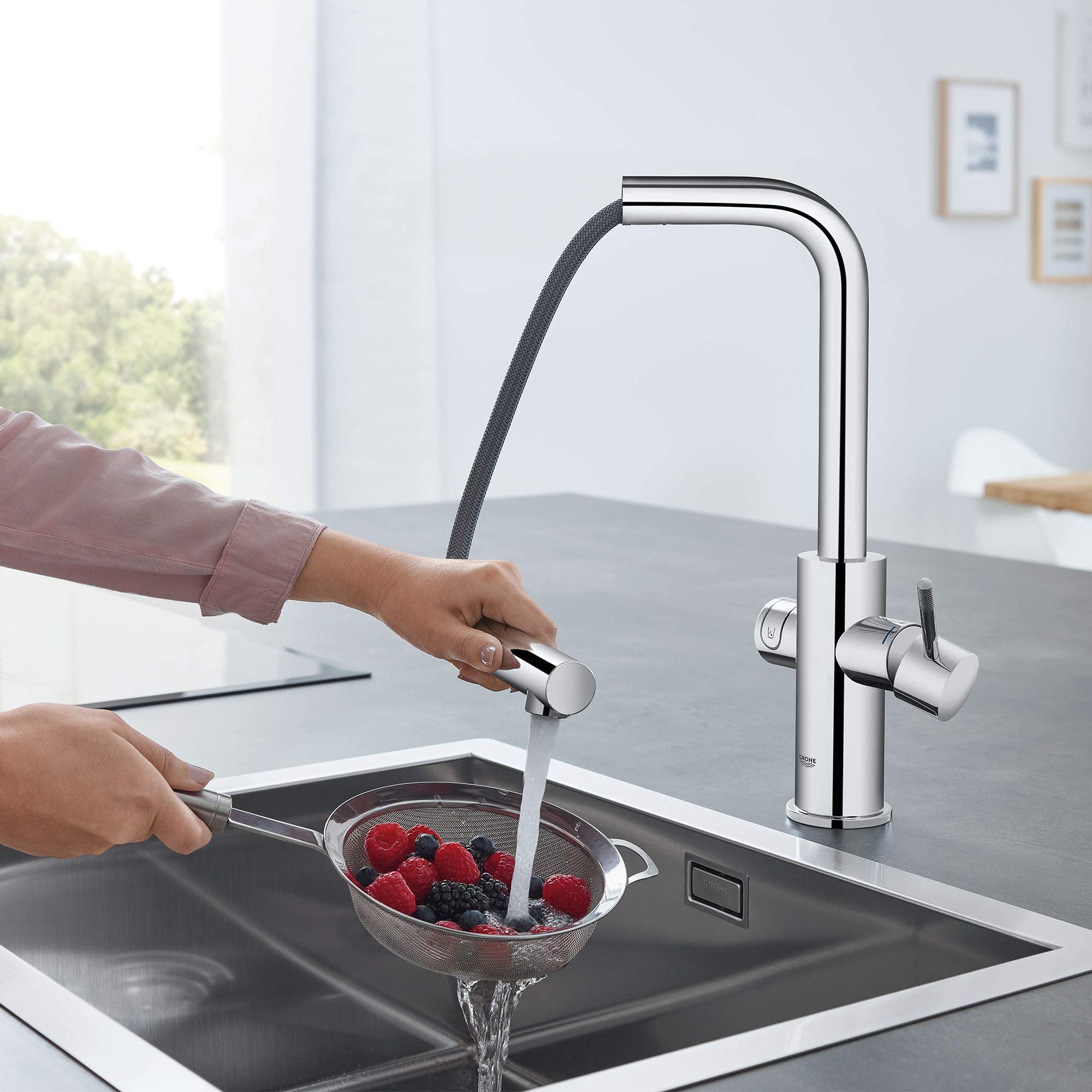 Chrome single-handle pull-out kitchen faucet with curved spout and flexible hose, shown dispensing water into a colander of b