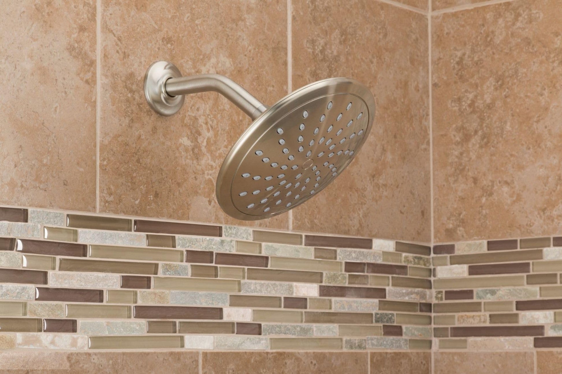 Brushed nickel rain shower head mounted on wall with curved arm, showing spray holes in circular face.