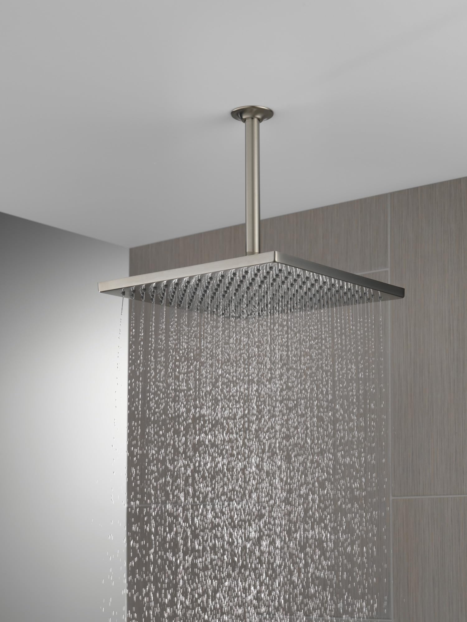 Stainless steel square raincan shower head with ceiling-mounted arm dispensing water in rain-like pattern.