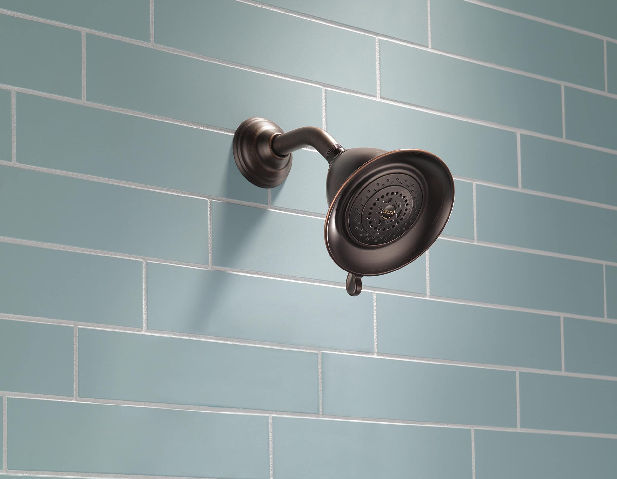 Chrome shower head with curved arm and round face mounted on tiled wall.
