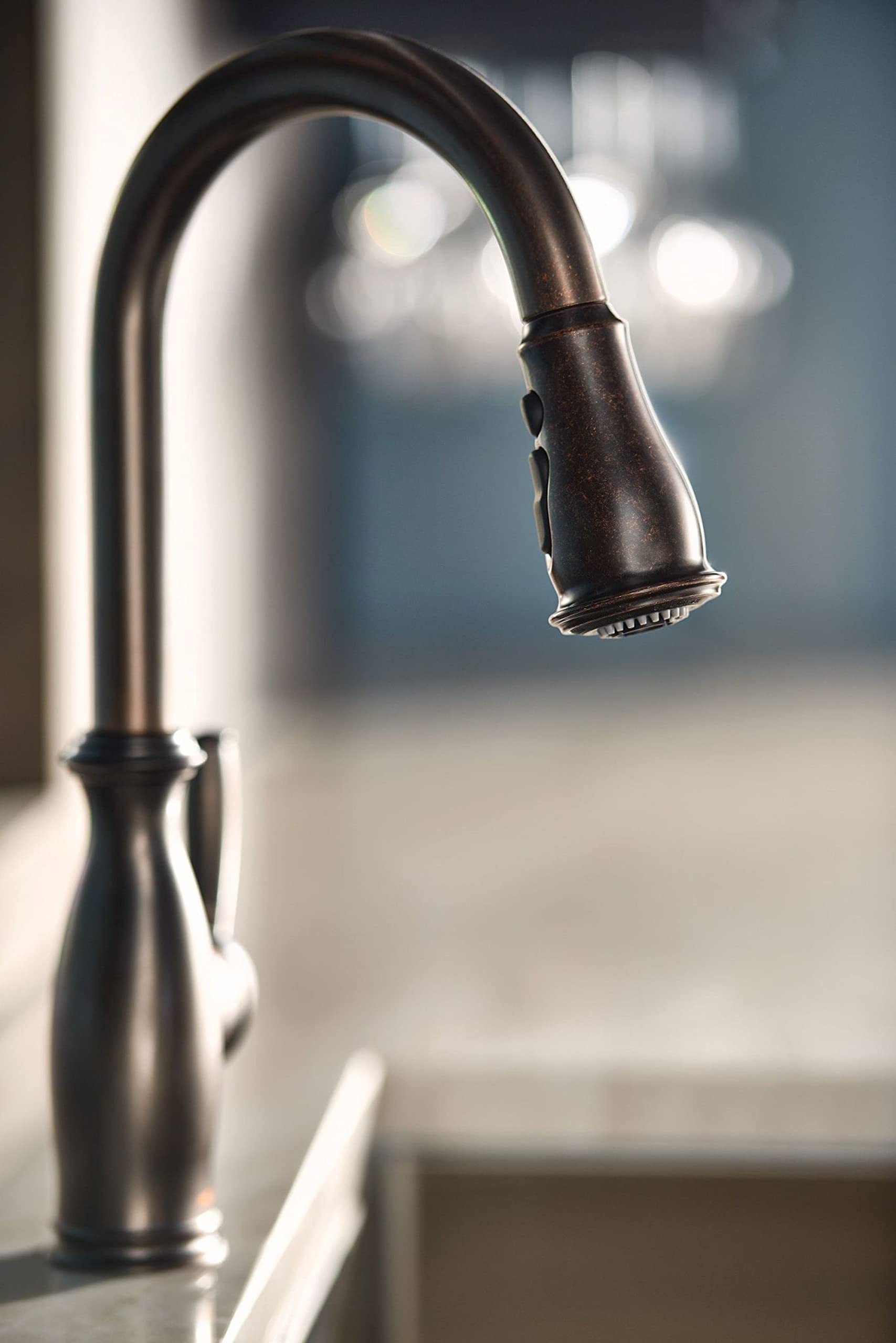 Oil rubbed bronze kitchen faucet with curved spout and pull-down spray head with side handle.