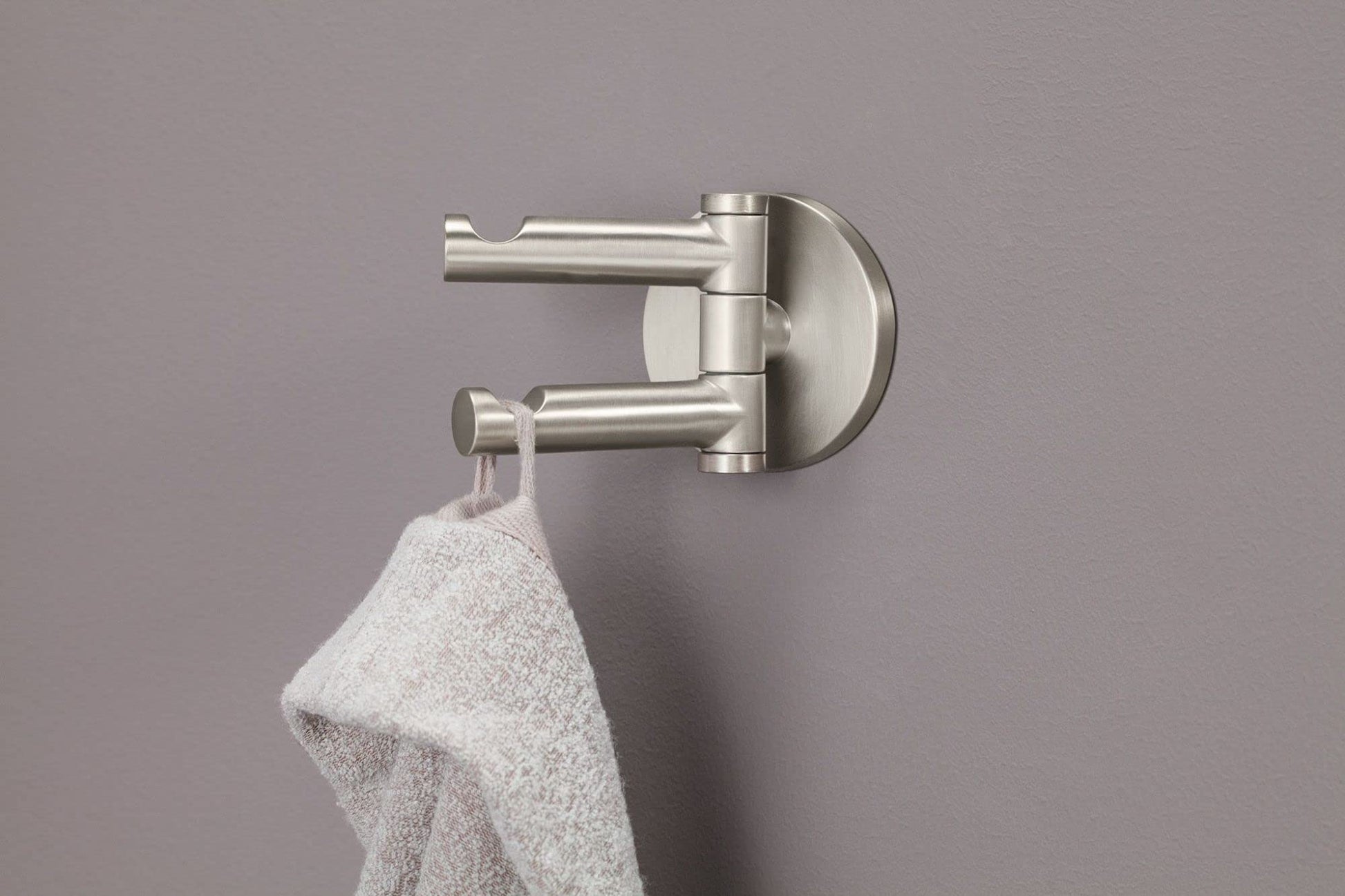 Brushed nickel double robe hook with two horizontal arms mounted on circular backing plate, holding white towel.