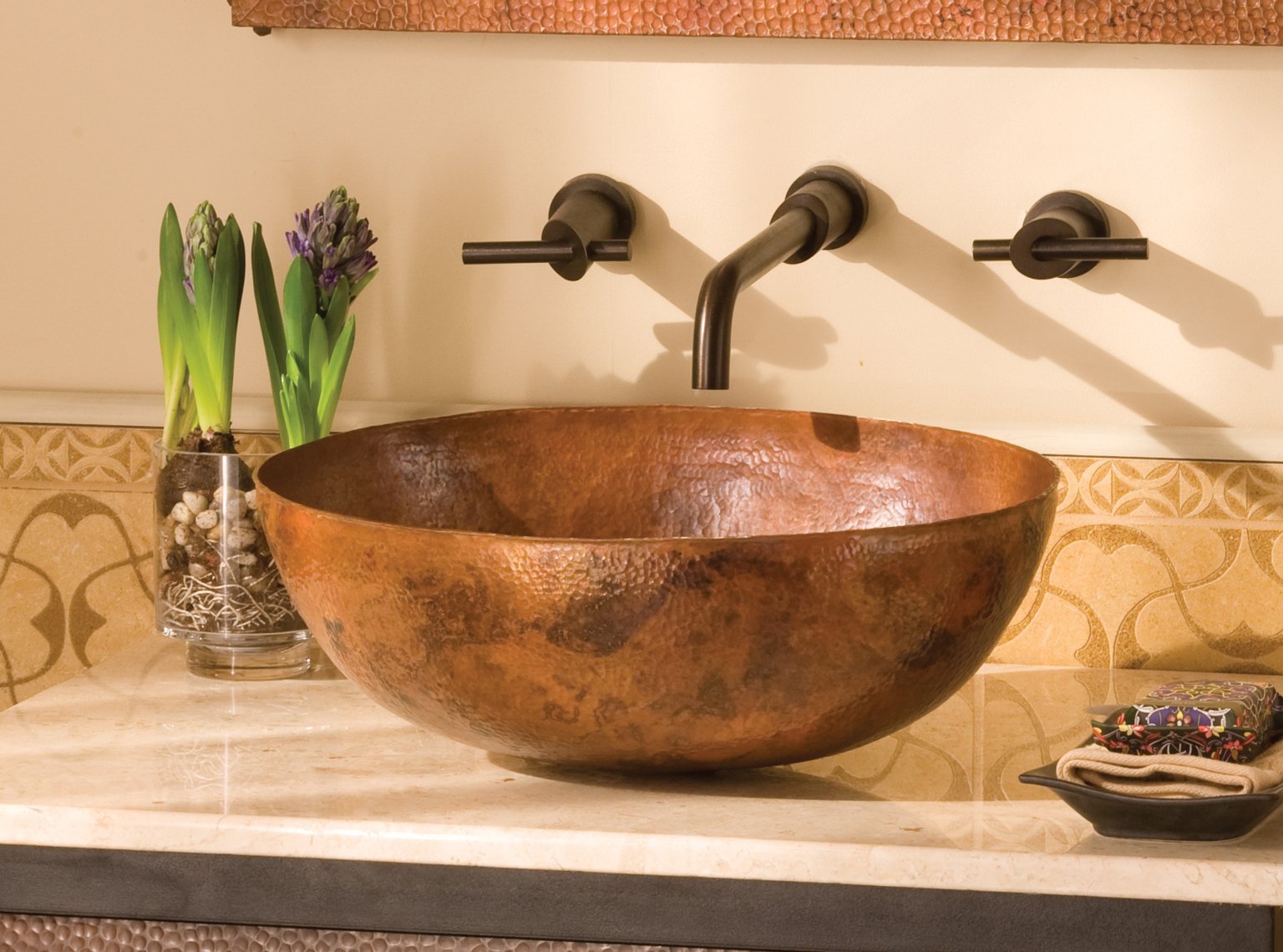 Hammered copper oval vessel sink with textured surface on bathroom counter with wall-mounted faucet.