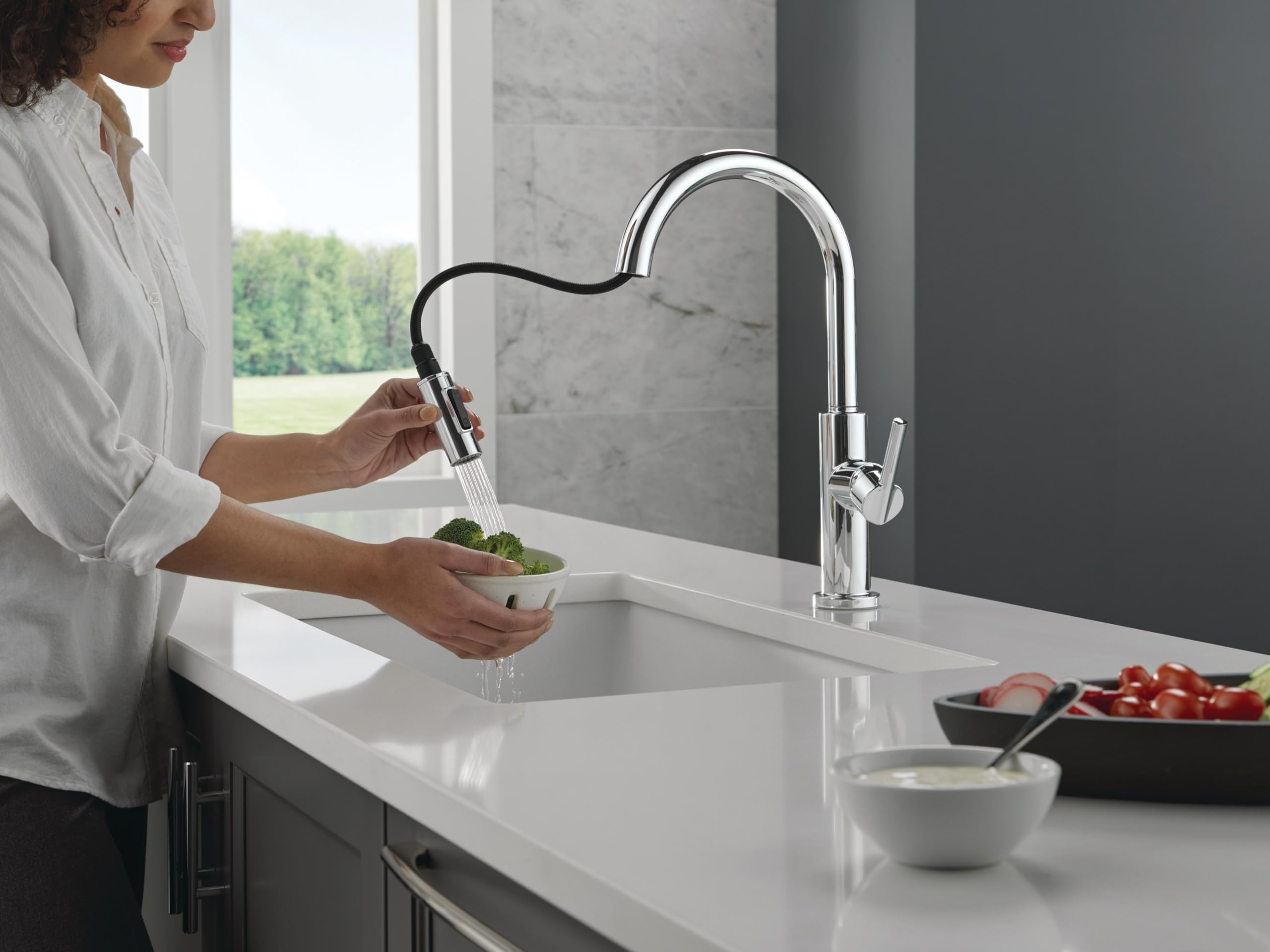Chrome pull-down kitchen faucet with single handle, flexible hose extended over white sink basin.