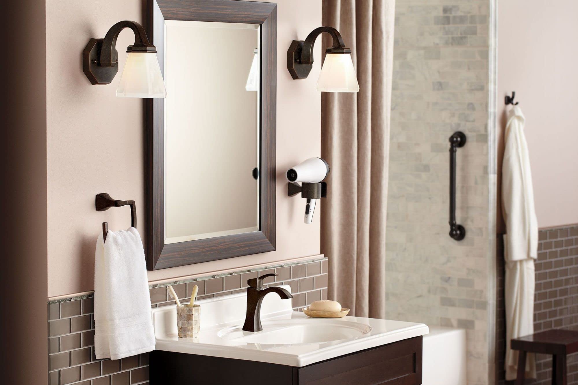 Moen double robe hook in bronze finish mounted on bathroom wall beside mirror.