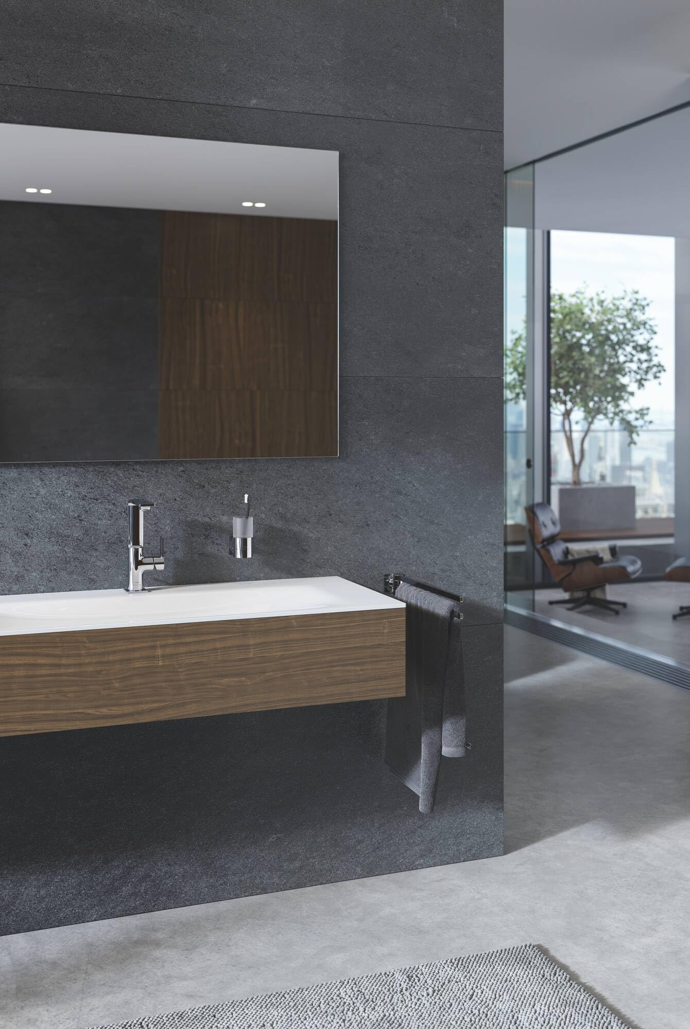 Chrome soap dispenser mounted on dark gray bathroom wall next to sink.