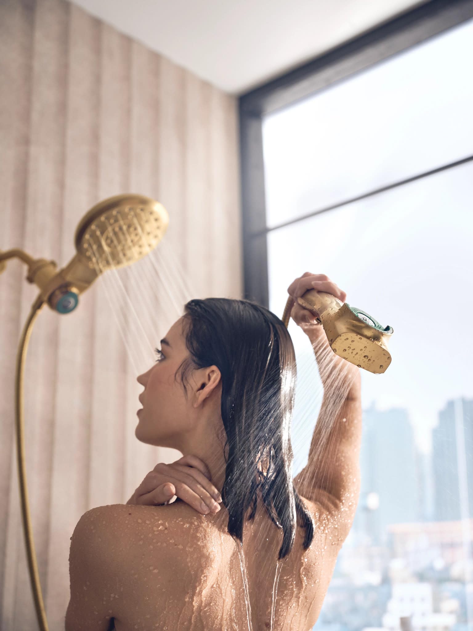 Brushed gold shower system with overhead rainfall showerhead and handheld wand mounted on bathroom wall.