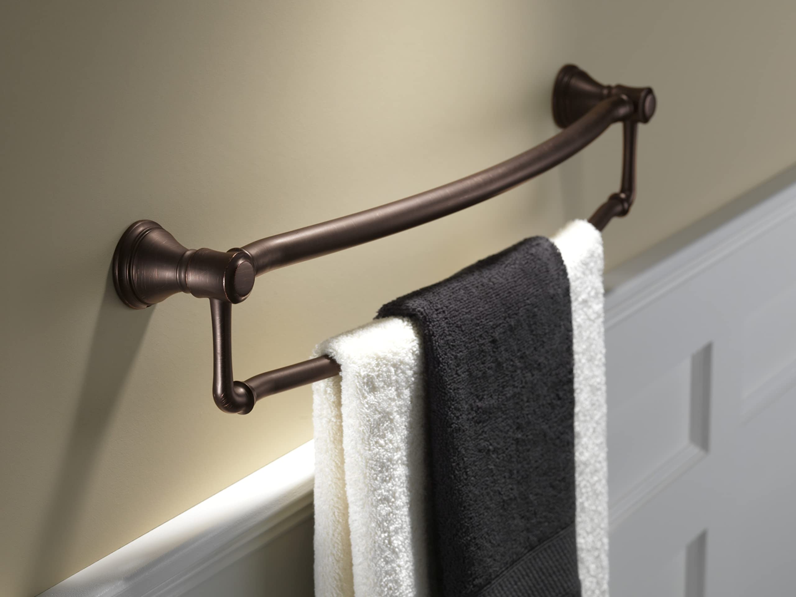 Oil-rubbed bronze curved towel bar with assist grab rail mounted on beige wall, holding folded white and dark towels.