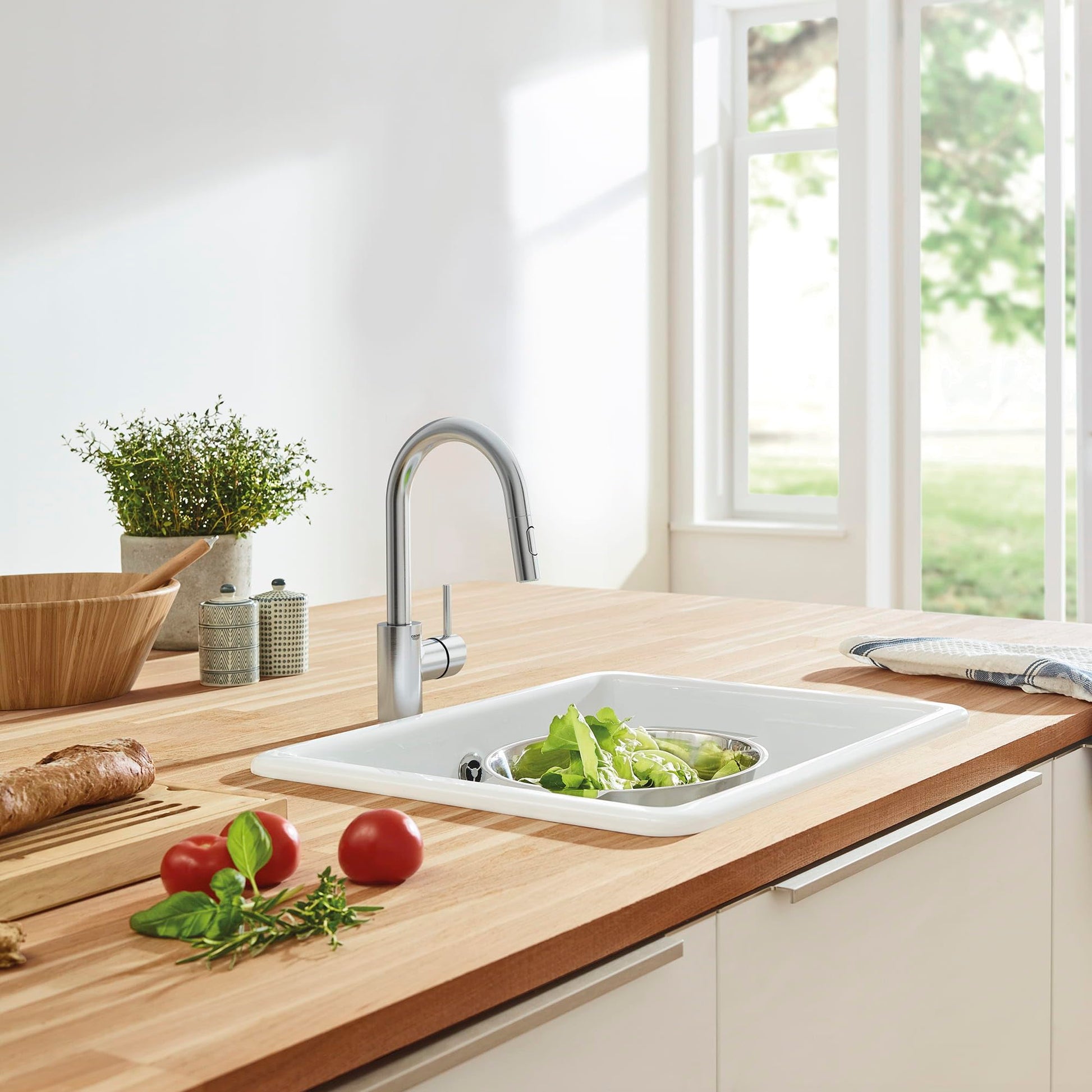 Stainless steel single-handle pull-down bar faucet with curved spout installed above white rectangular kitchen sink.