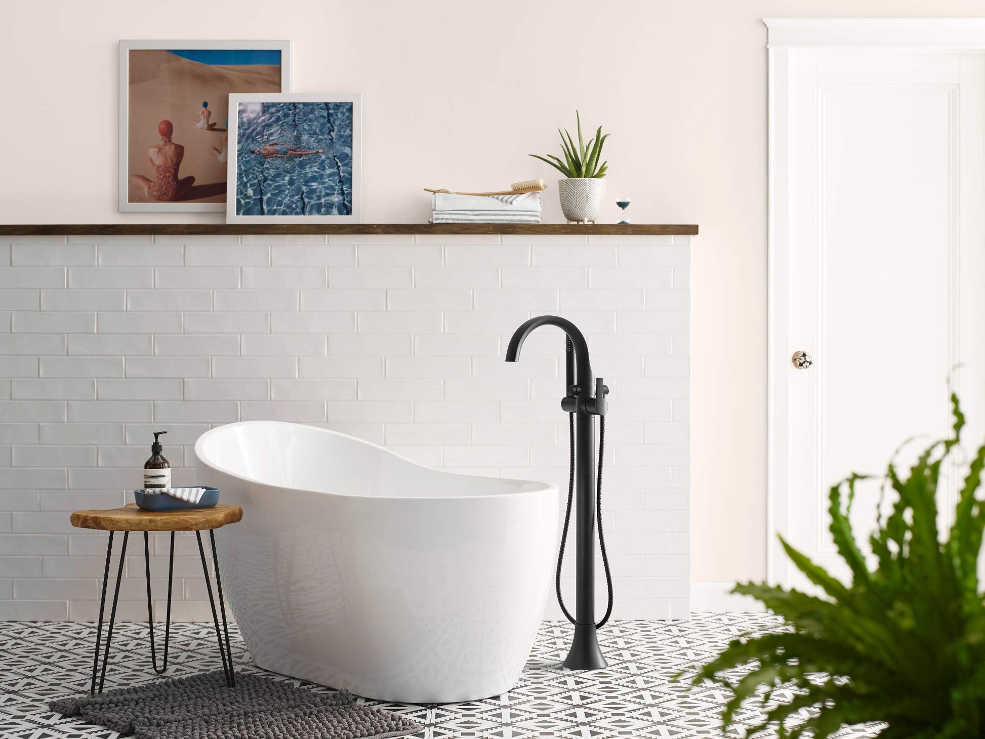 Chrome freestanding floor mount tub filler with single handle and detachable handshower, displayed next to white soaking tub.