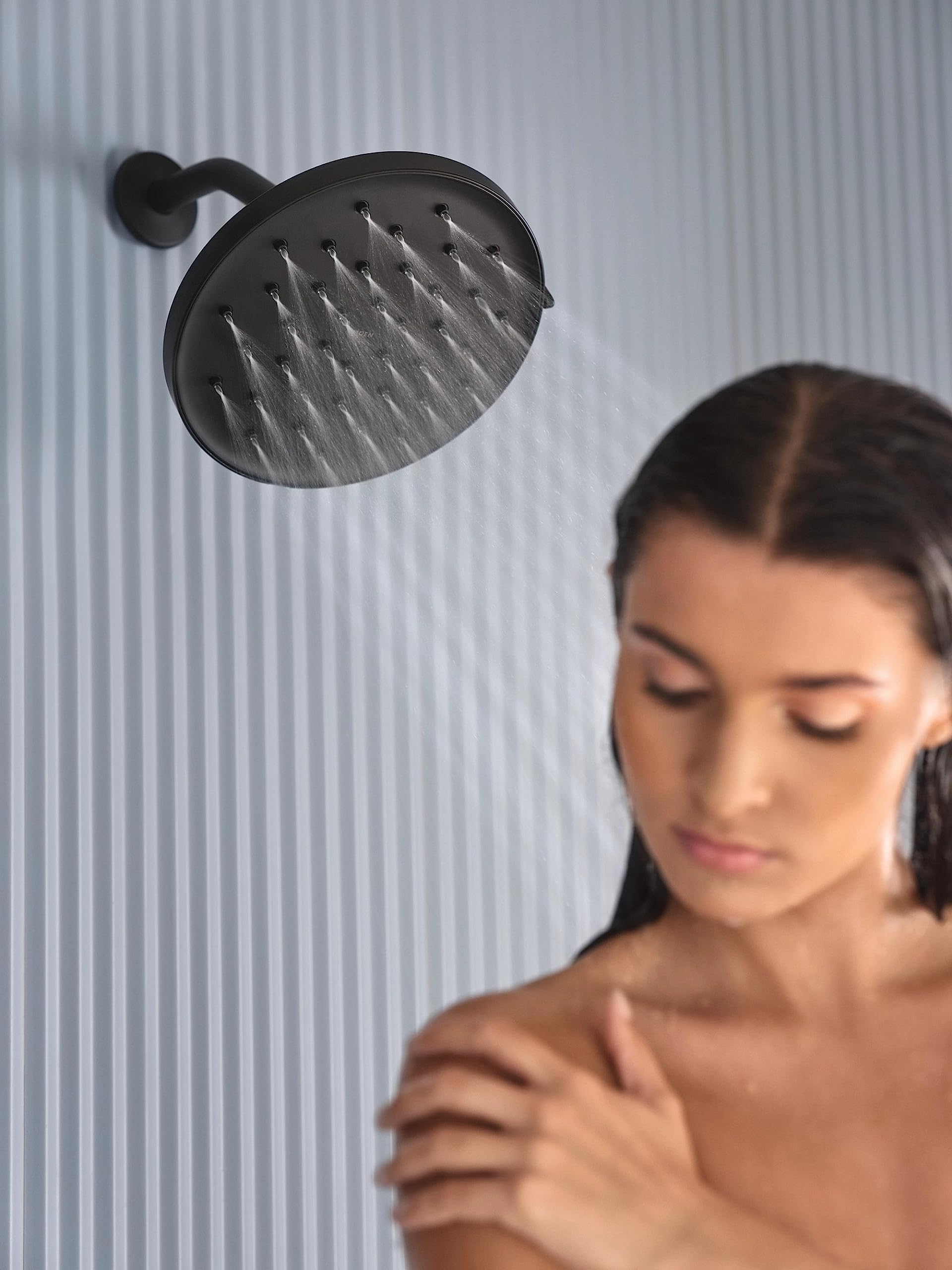 Matte black round rainshower head mounted on wall with water streaming downward.