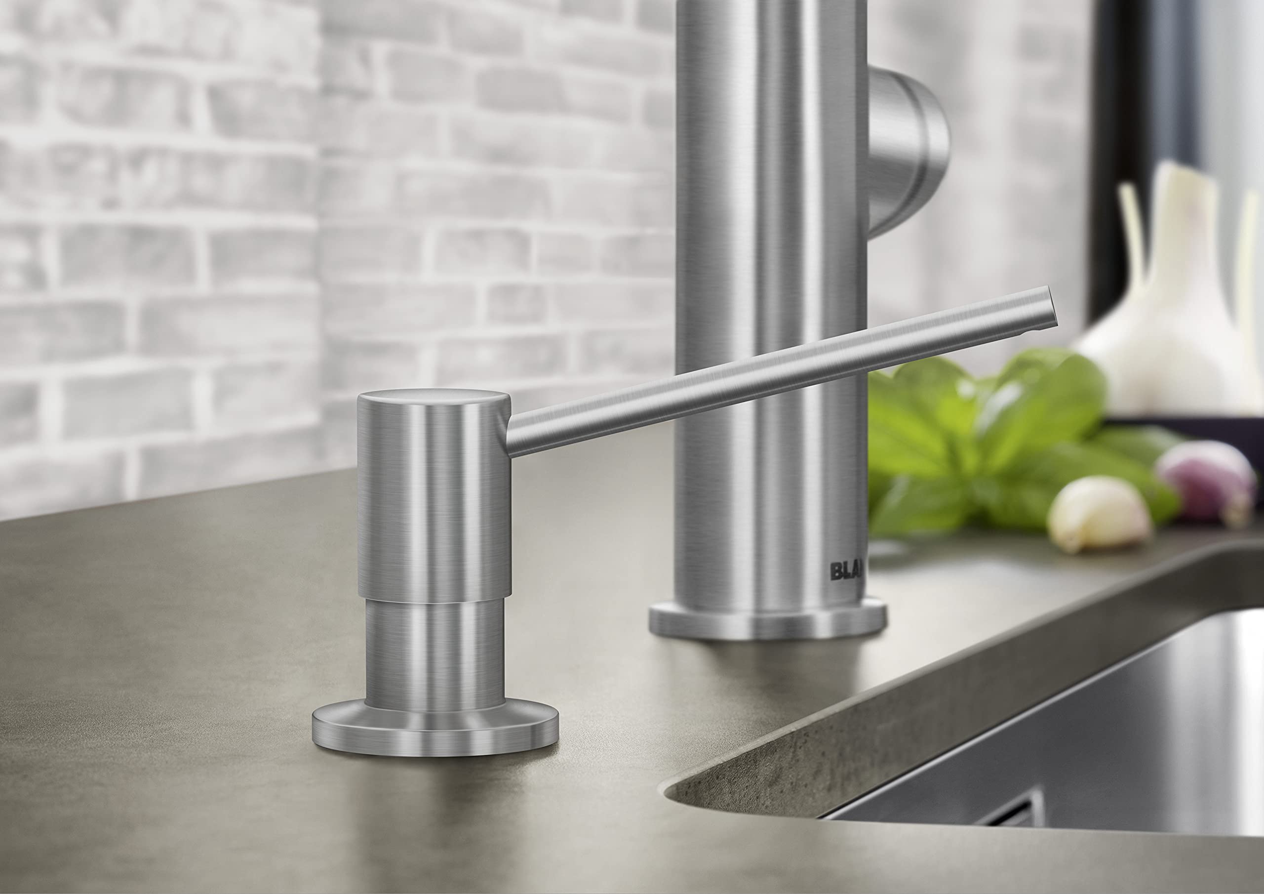 Satin dark steel soap dispenser with cylindrical pump mounted on kitchen countertop next to sink faucet.
