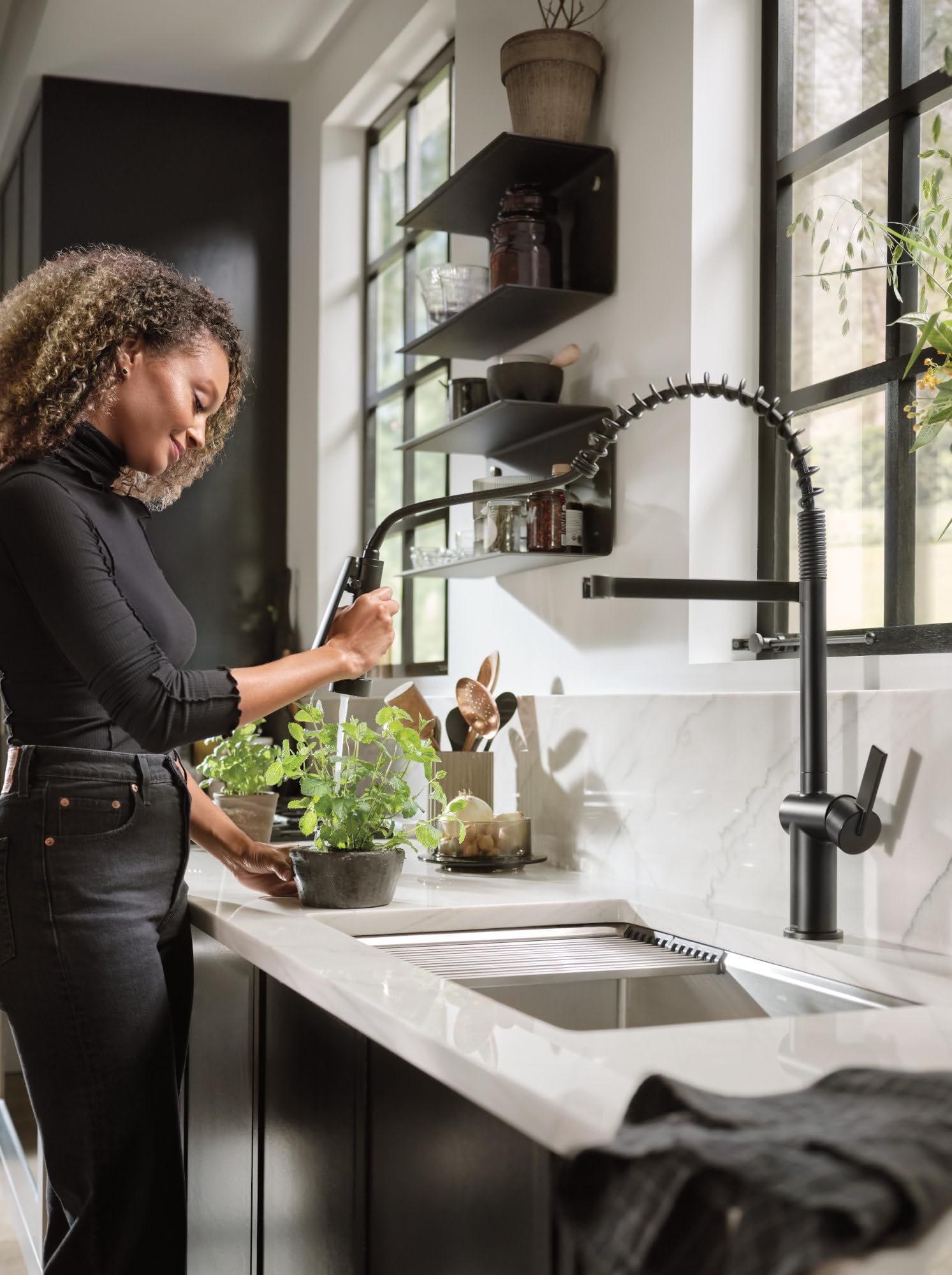 Matte black pre-rinse spring kitchen faucet with coiled hose and handle installed above white sink counter.