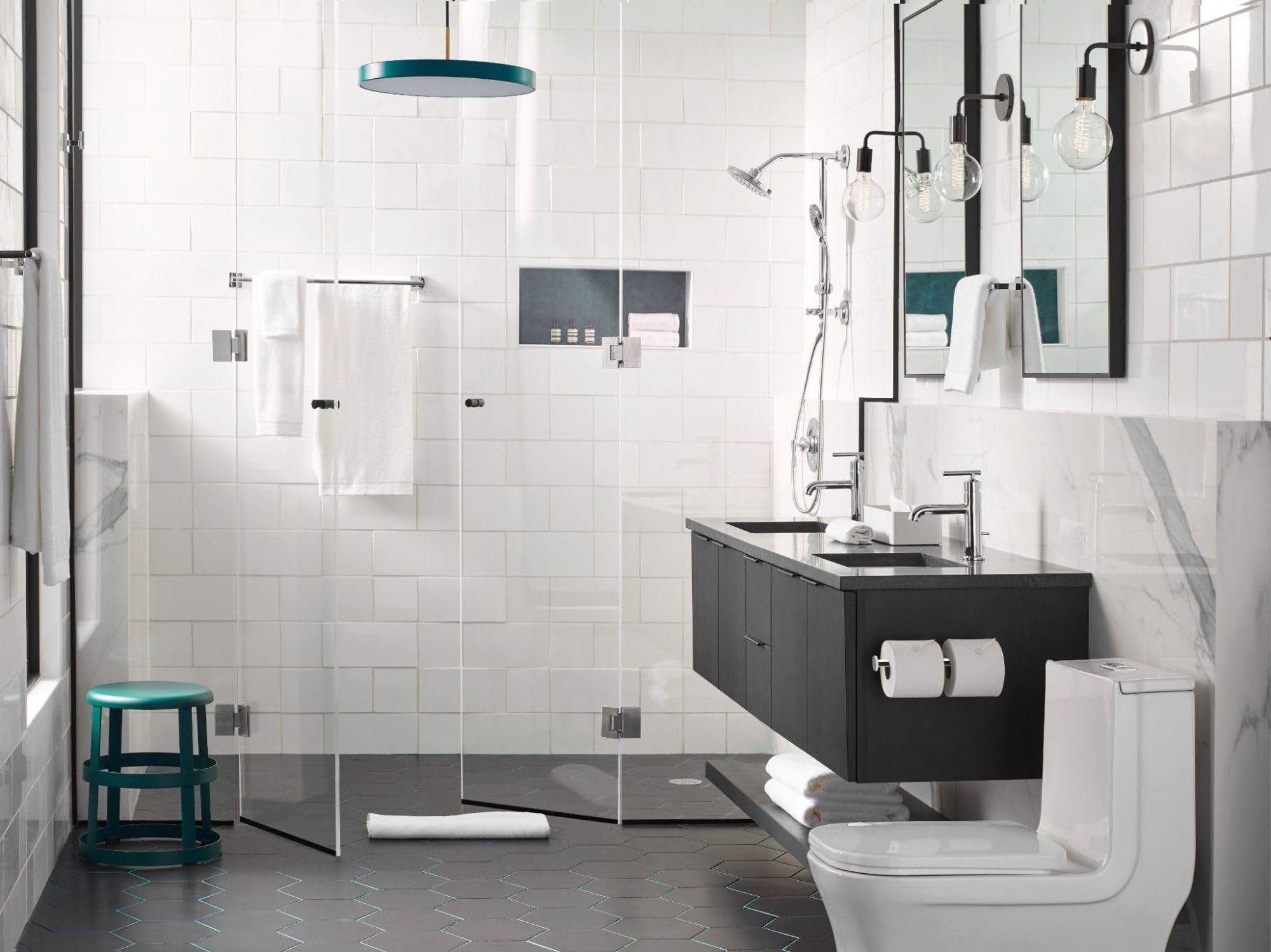 Chrome shower trim kit with single handle mounted on white tiled bathroom wall above glass shower enclosure.