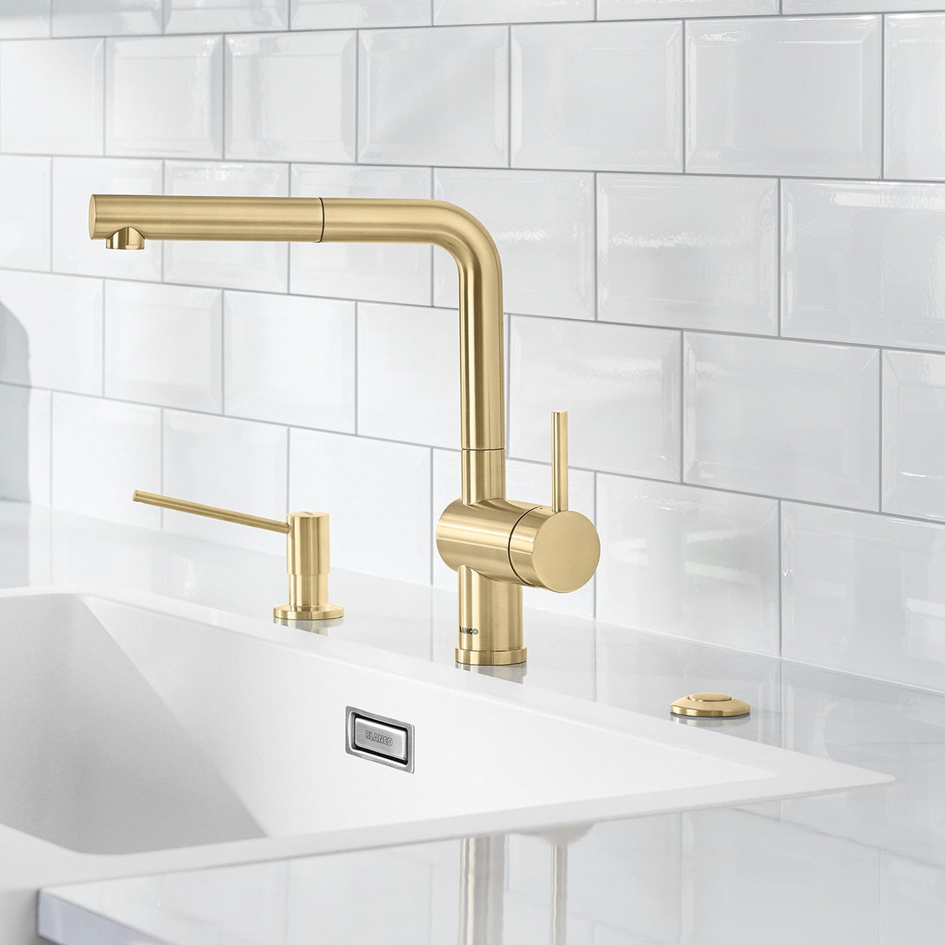 Satin gold kitchen faucet with pull-down spout and matching soap dispenser on white countertop.