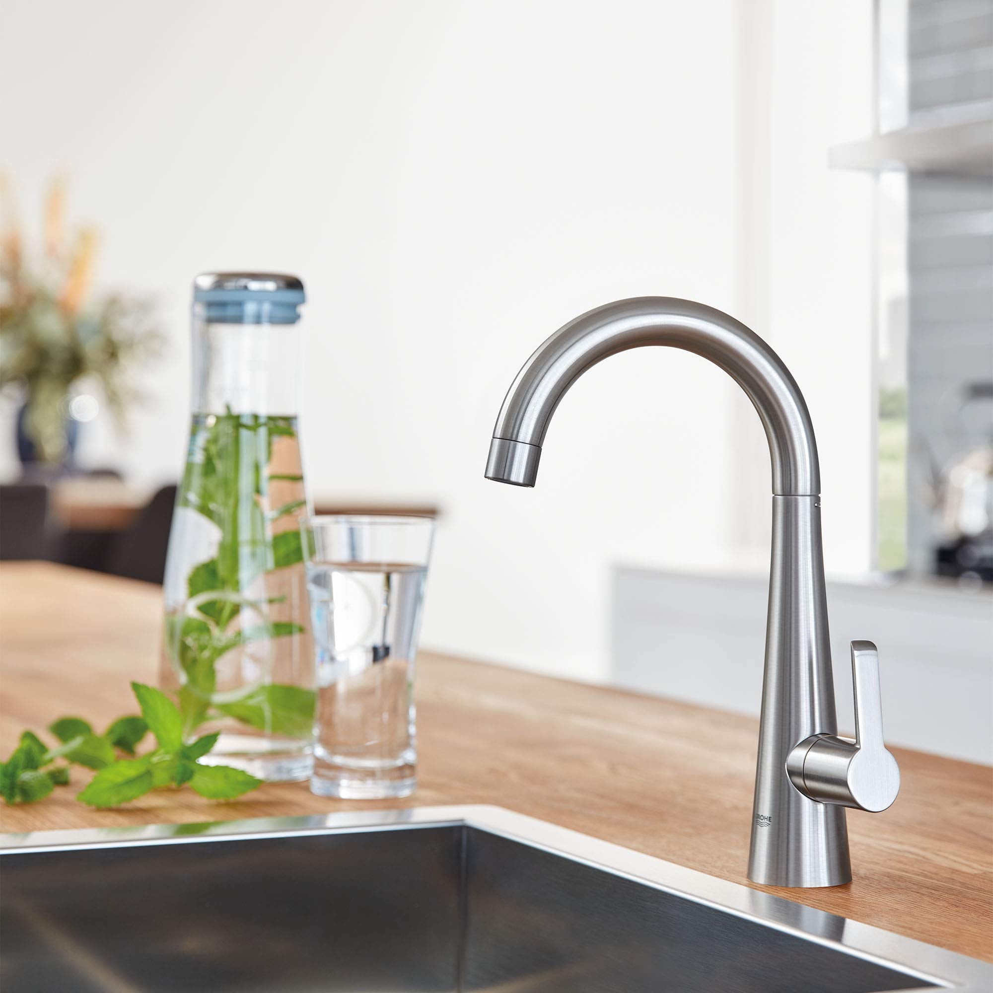 Stainless steel single-handle beverage faucet with curved spout and white lever handle mounted on wooden countertop.