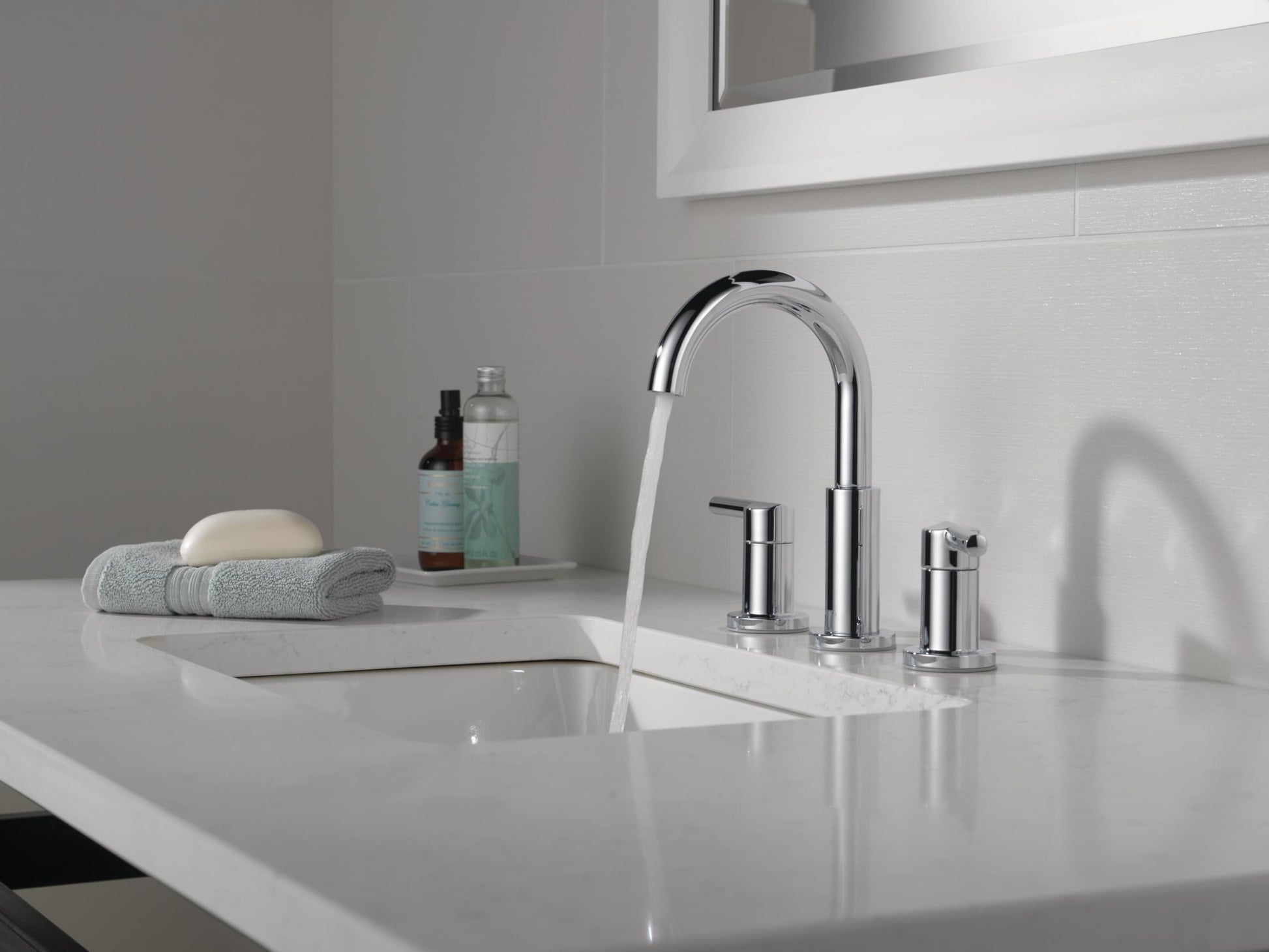 Chrome two-handle widespread bathroom faucet with curved spout and cylindrical handles on white sink countertop.