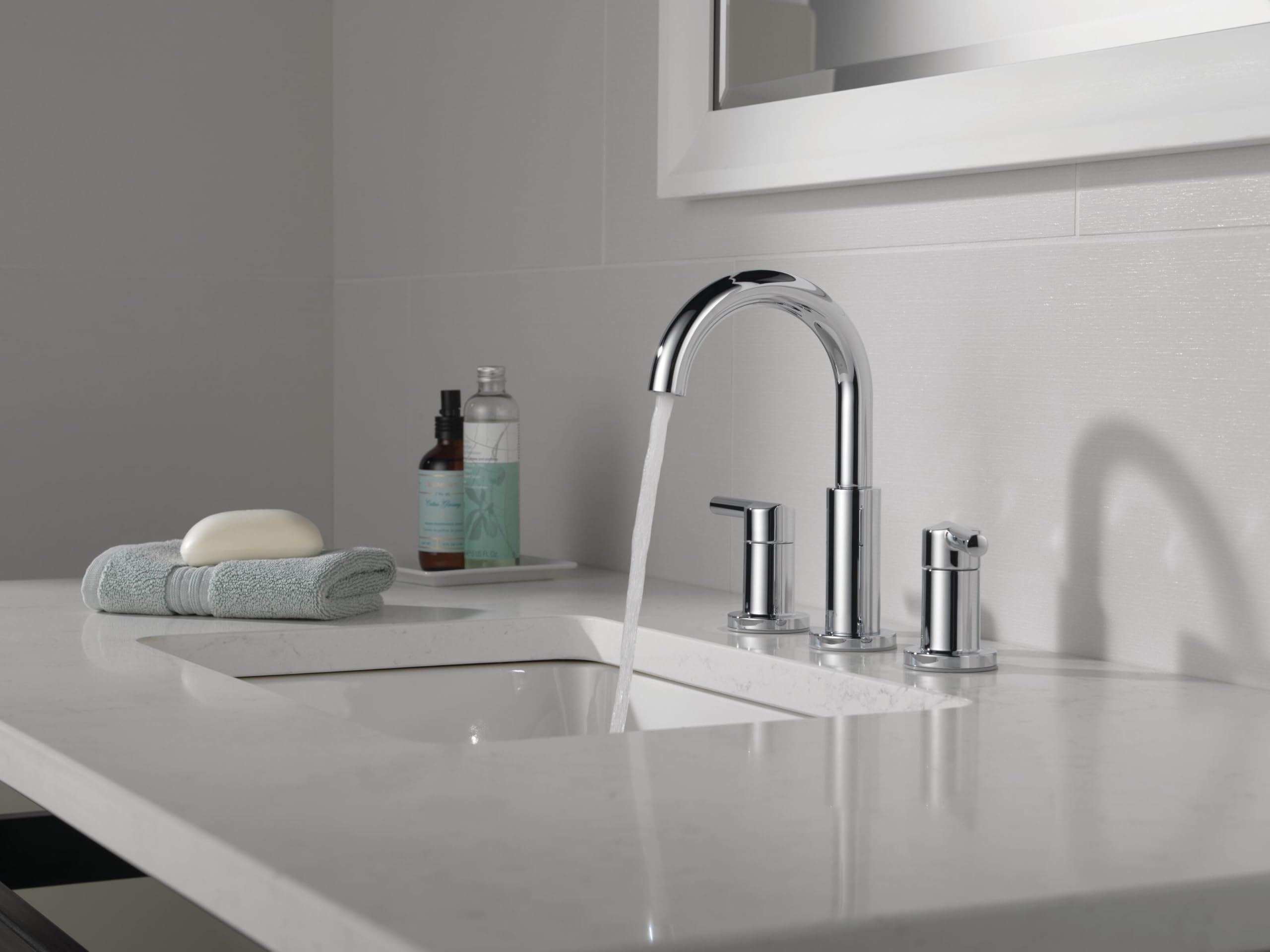 Chrome two-handle widespread bathroom faucet with curved spout and cylindrical handles on white sink countertop.