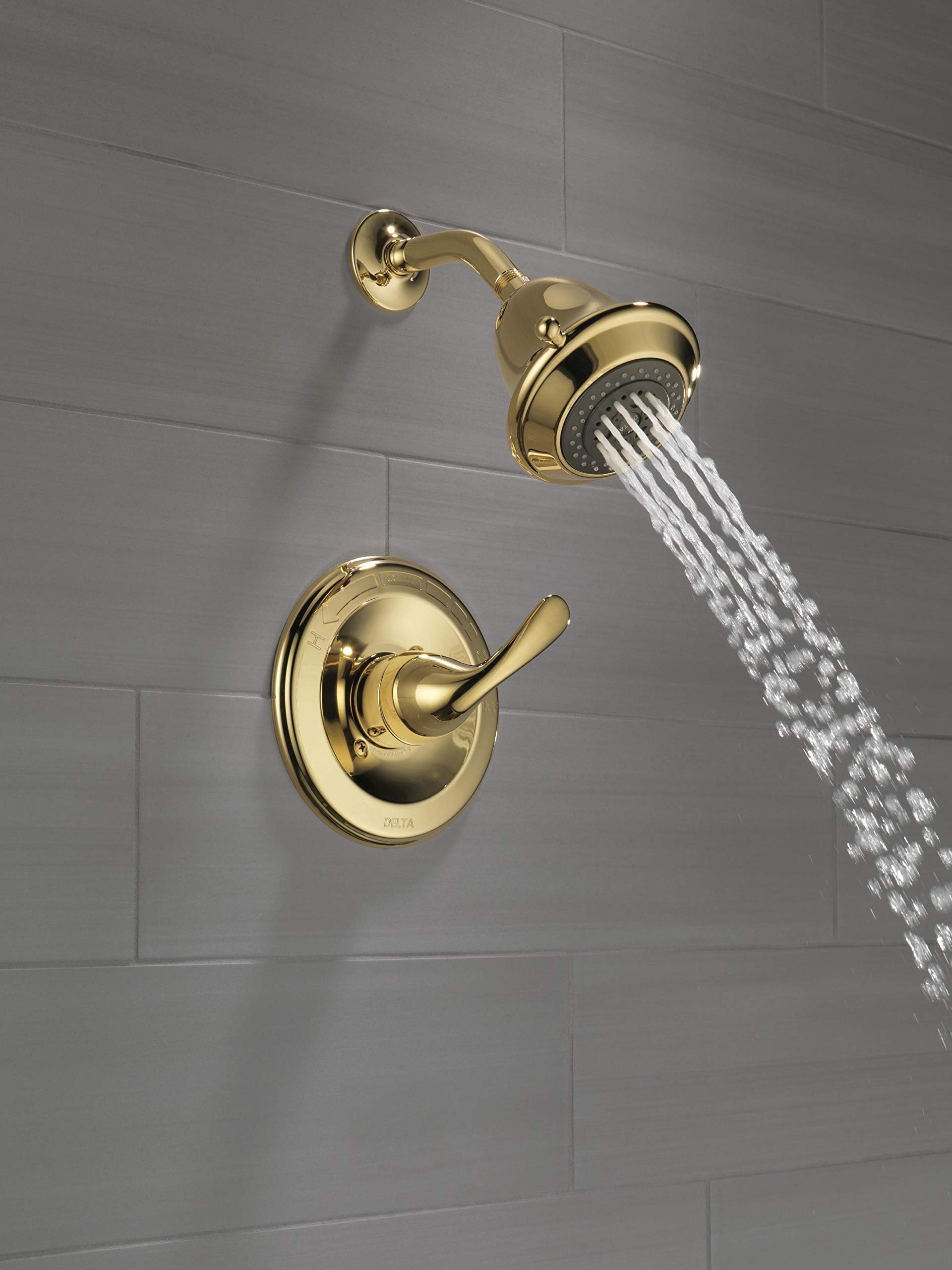 Polished brass shower trim with single lever handle and overhead showerhead mounted on tile wall with water stream visible.
