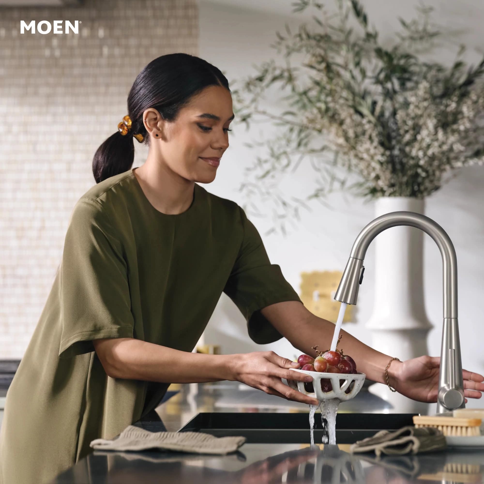 Stainless steel pull-down kitchen faucet with curved spout, shown rinsing produce in a sink.