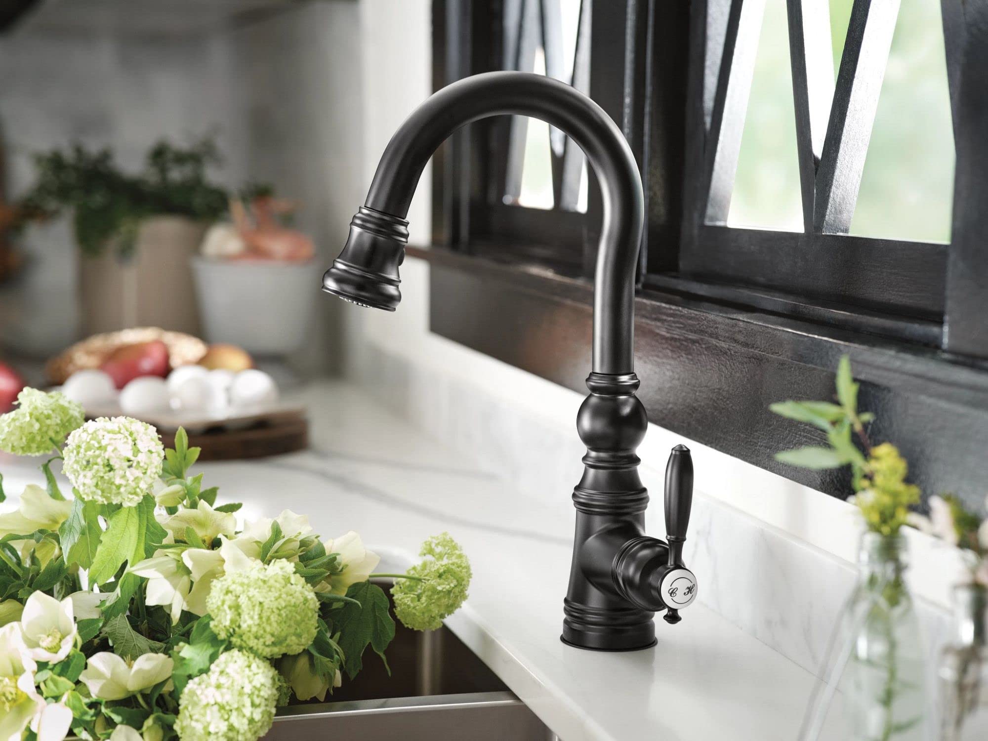 Matte black single-handle pulldown bar faucet with curved spout and decorative base installed over kitchen sink.