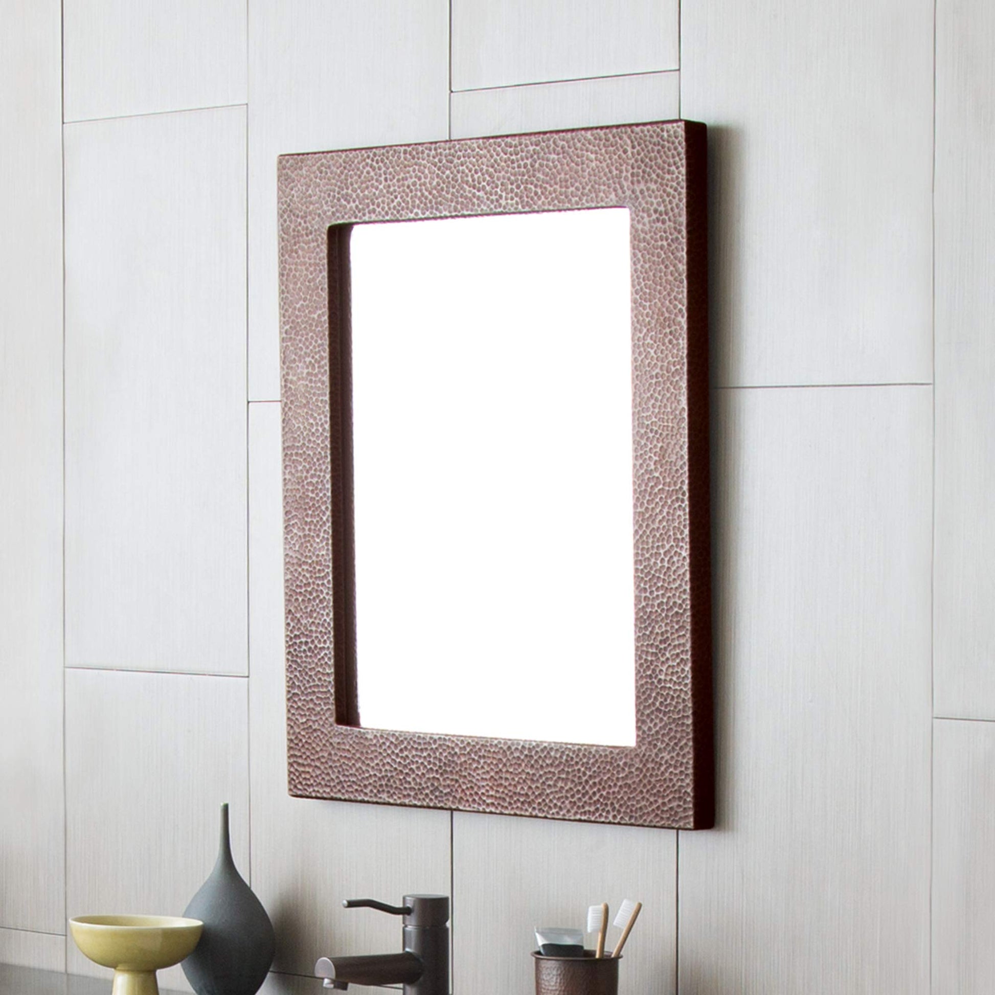 Rectangular mirror with textured copper-tone frame mounted on white tile wall above bathroom vanity.