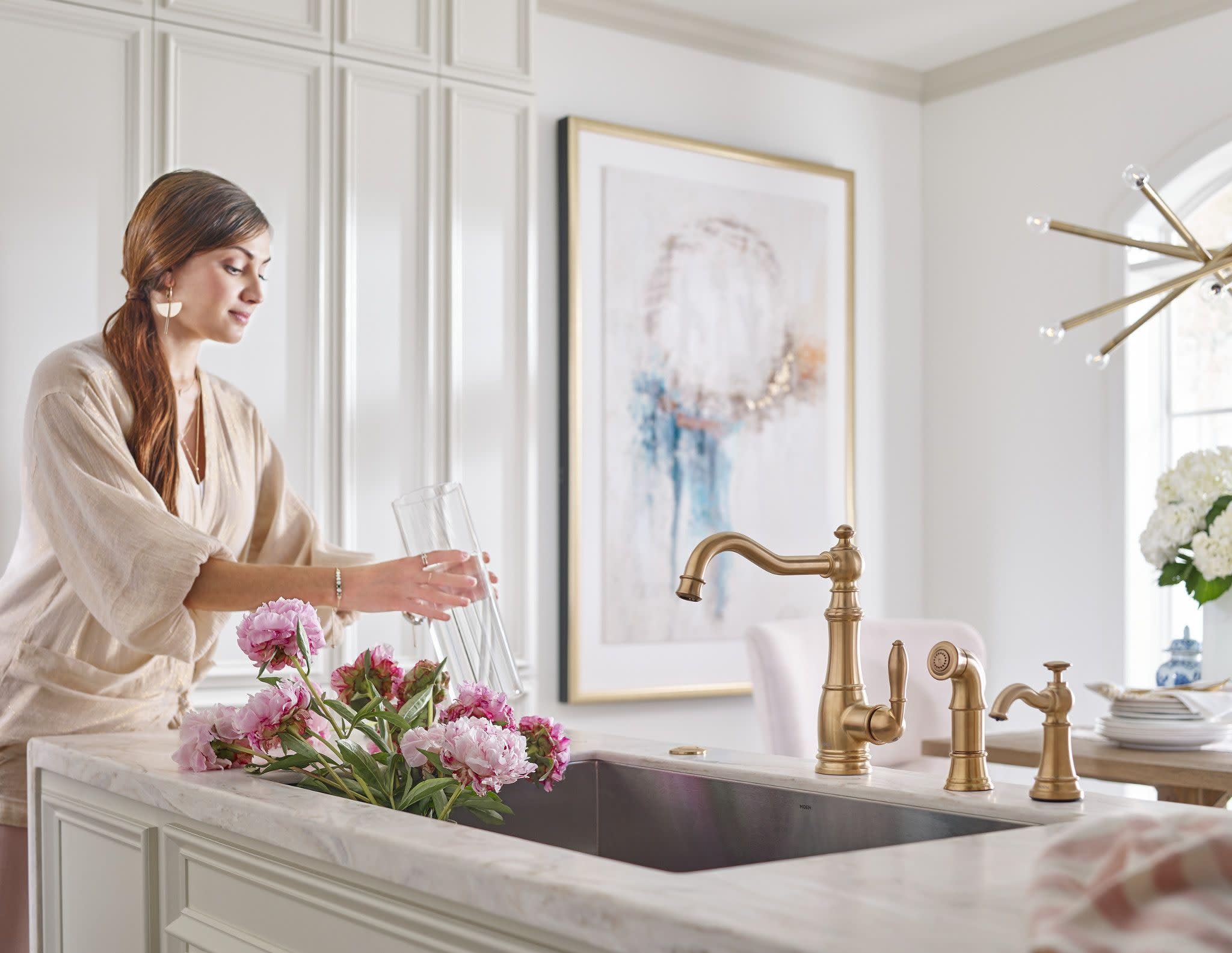 Brushed gold deck-mounted kitchen soap dispenser installed beside sink faucet with refillable bottle mounted above.