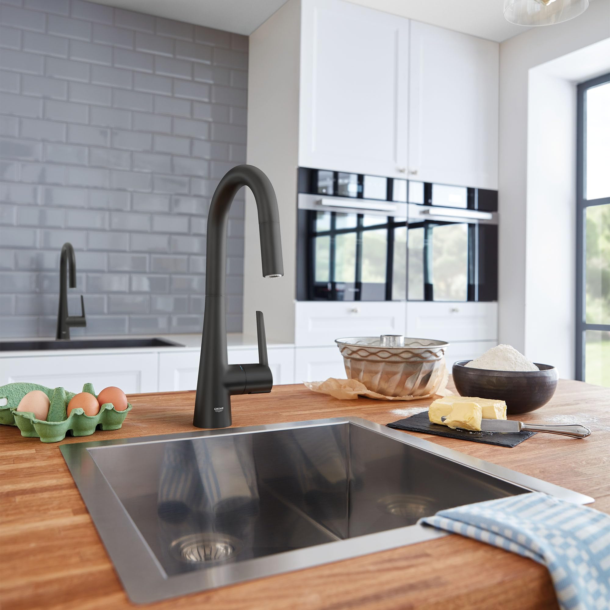 Matte black single-handle pull-down kitchen faucet with curved spout installed above stainless steel sink.