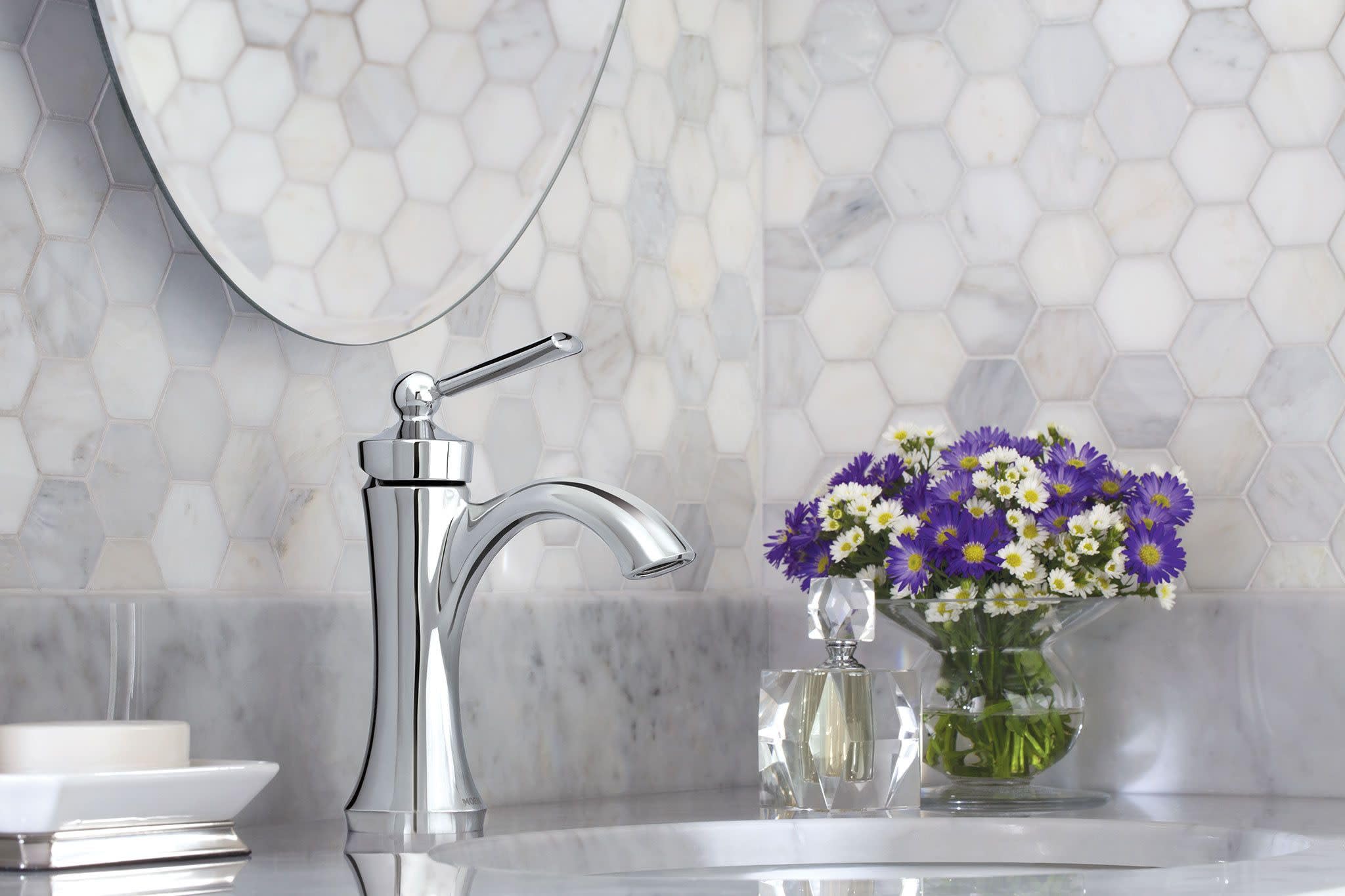 Brushed nickel single-handle high-arc bathroom faucet on marble countertop with hexagonal tile backsplash.
