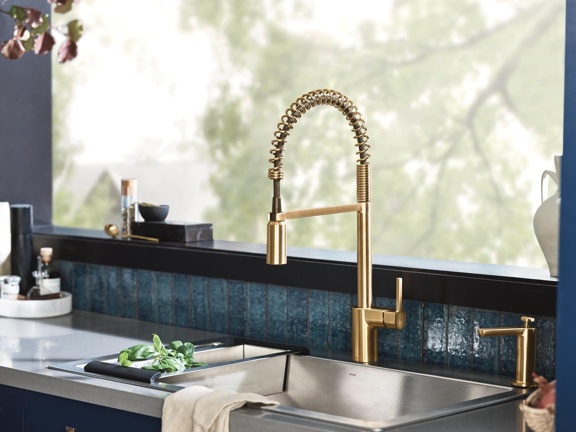 Brushed gold kitchen faucet with coiled spring spout and single handle mounted above stainless steel sink.