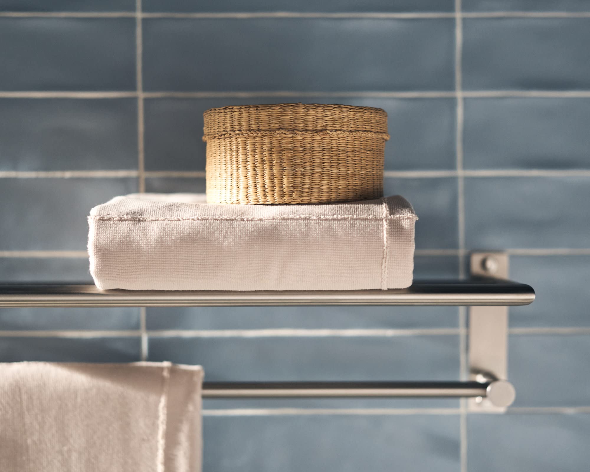 Brushed nickel towel shelf and bar with folded towel and woven basket on blue subway tile wall.