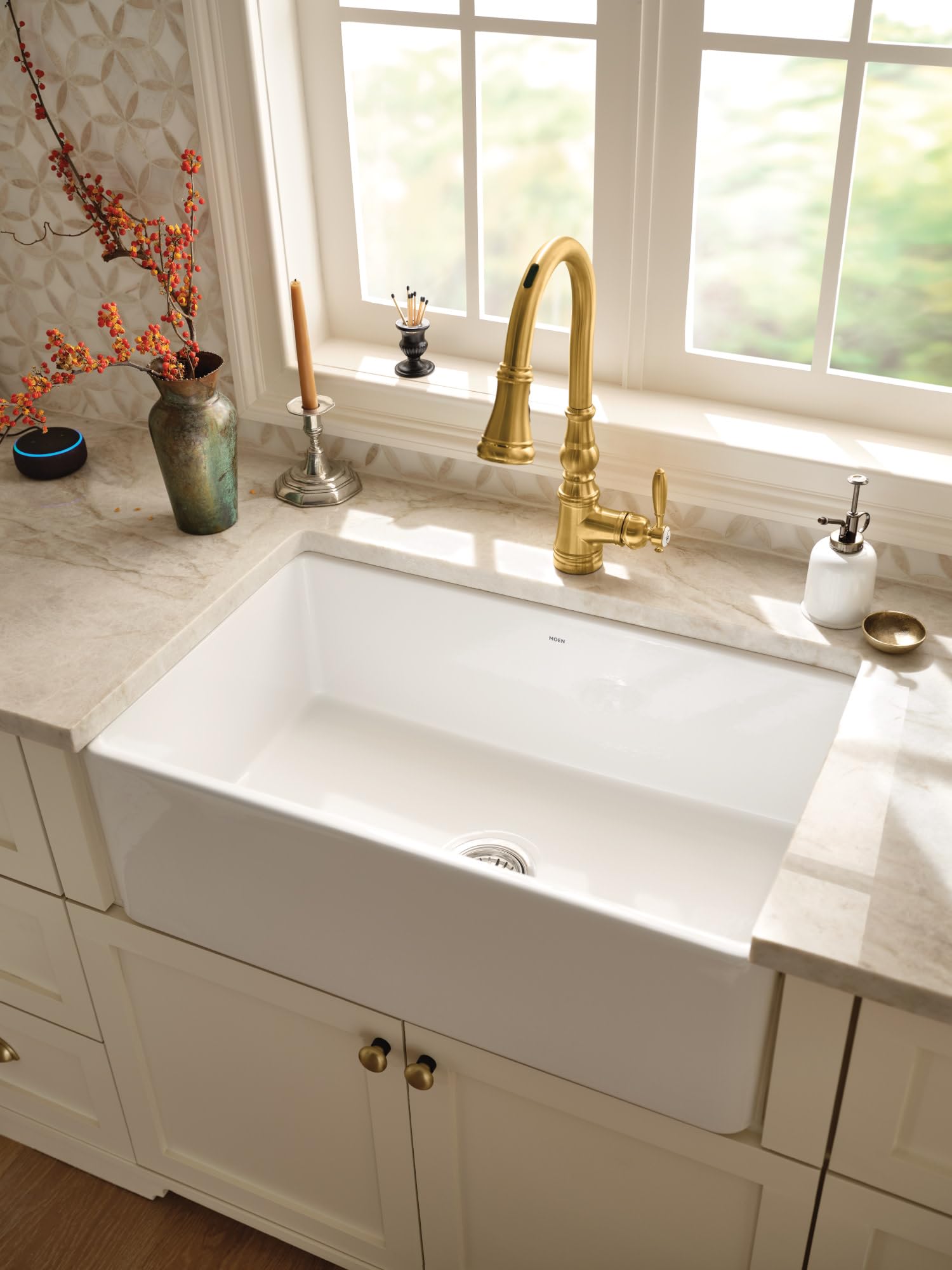 White fireclay apron front single bowl undermount sink installed in marble countertop with brass faucet.