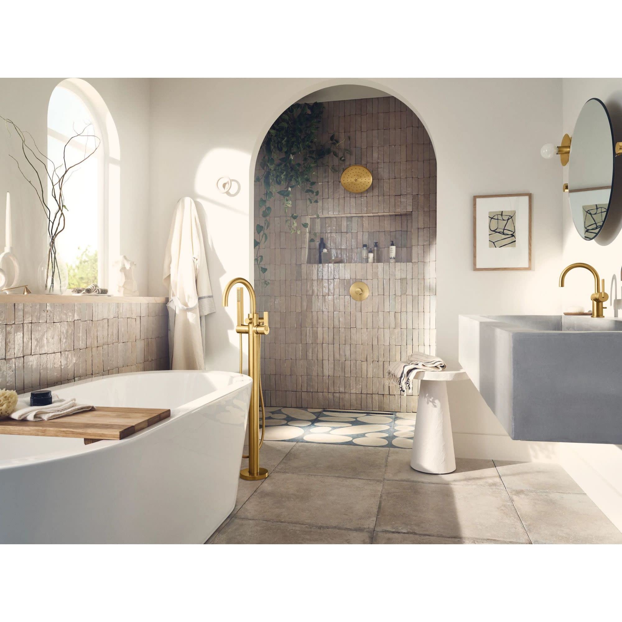 Chrome freestanding tub filler with single handle and attached handshower, displayed next to a white soaking tub in a bathroo