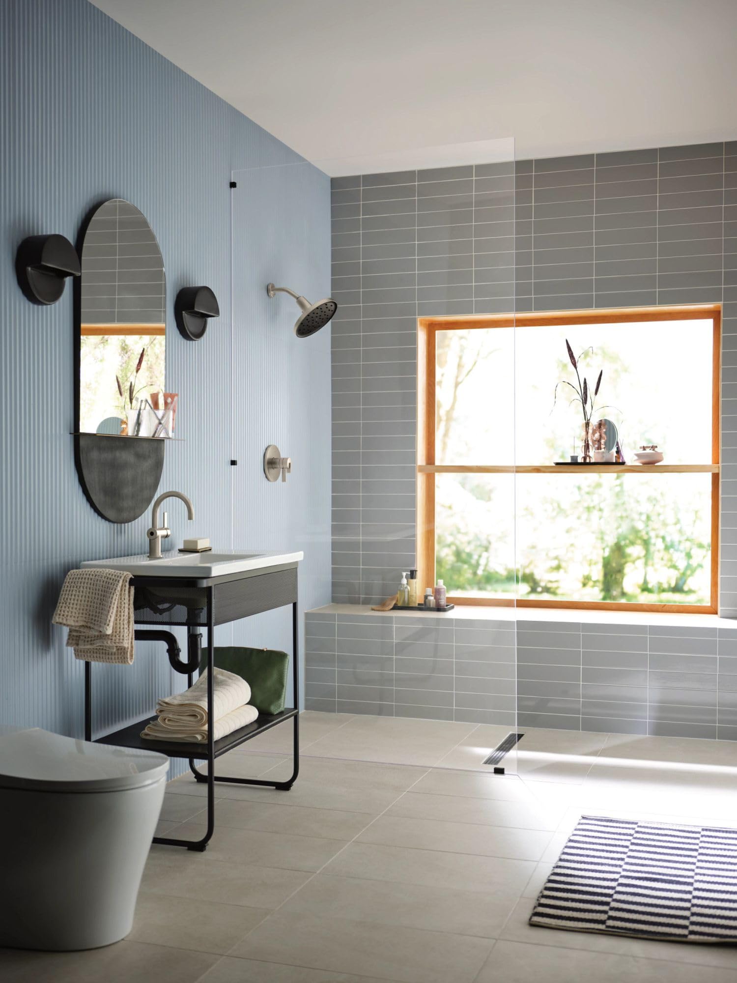 Brushed nickel circular rainshower spray head mounted above a bathtub in a modern bathroom with gray tile.