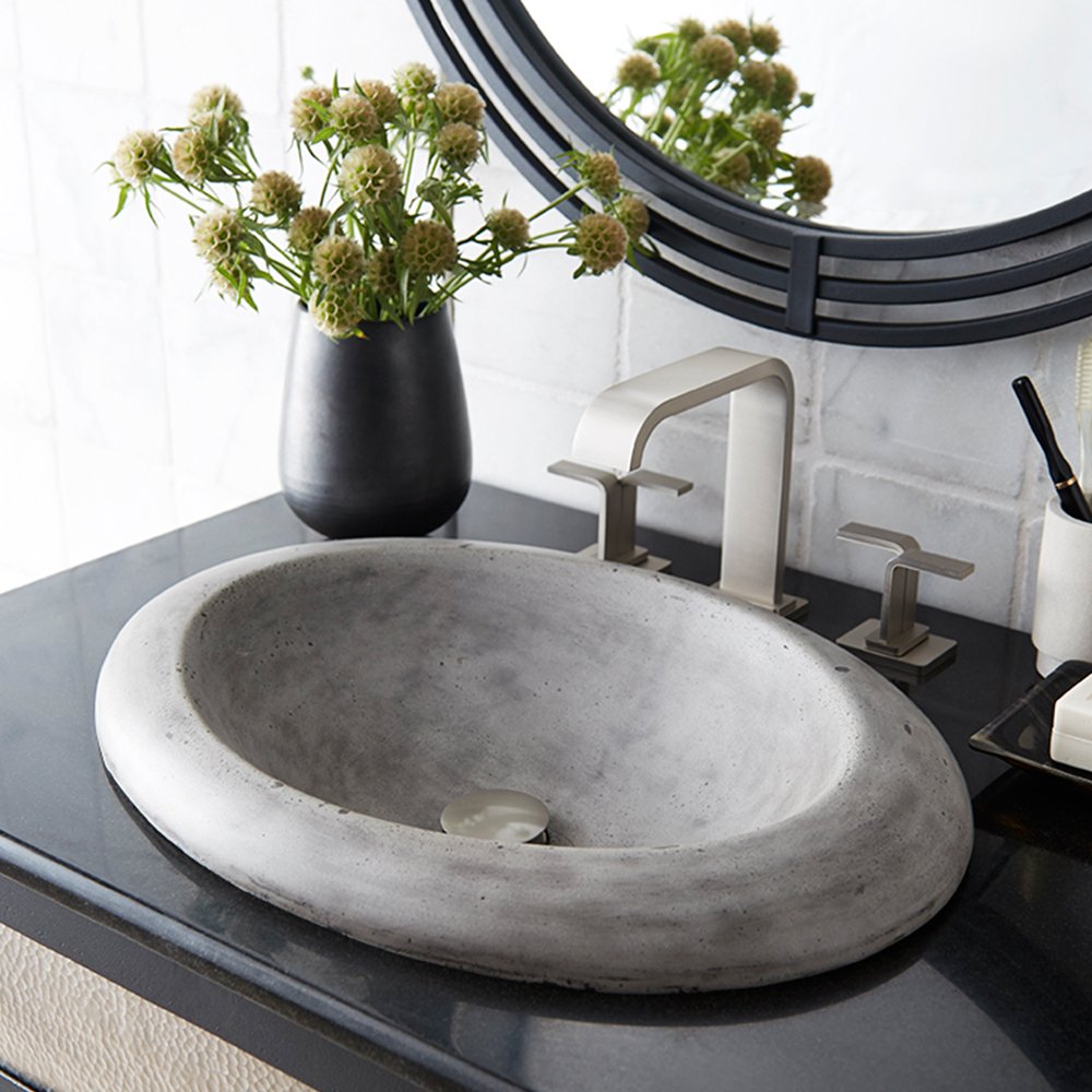 Oval concrete bathroom sink with smooth gray finish and rolled rim mounted on dark countertop.