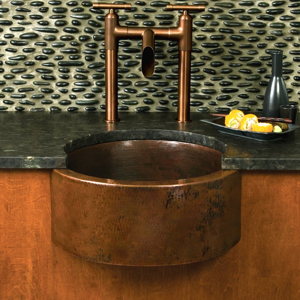 Hammered copper undermount bar sink with textured surface installed beneath dark countertop with matching copper faucet.